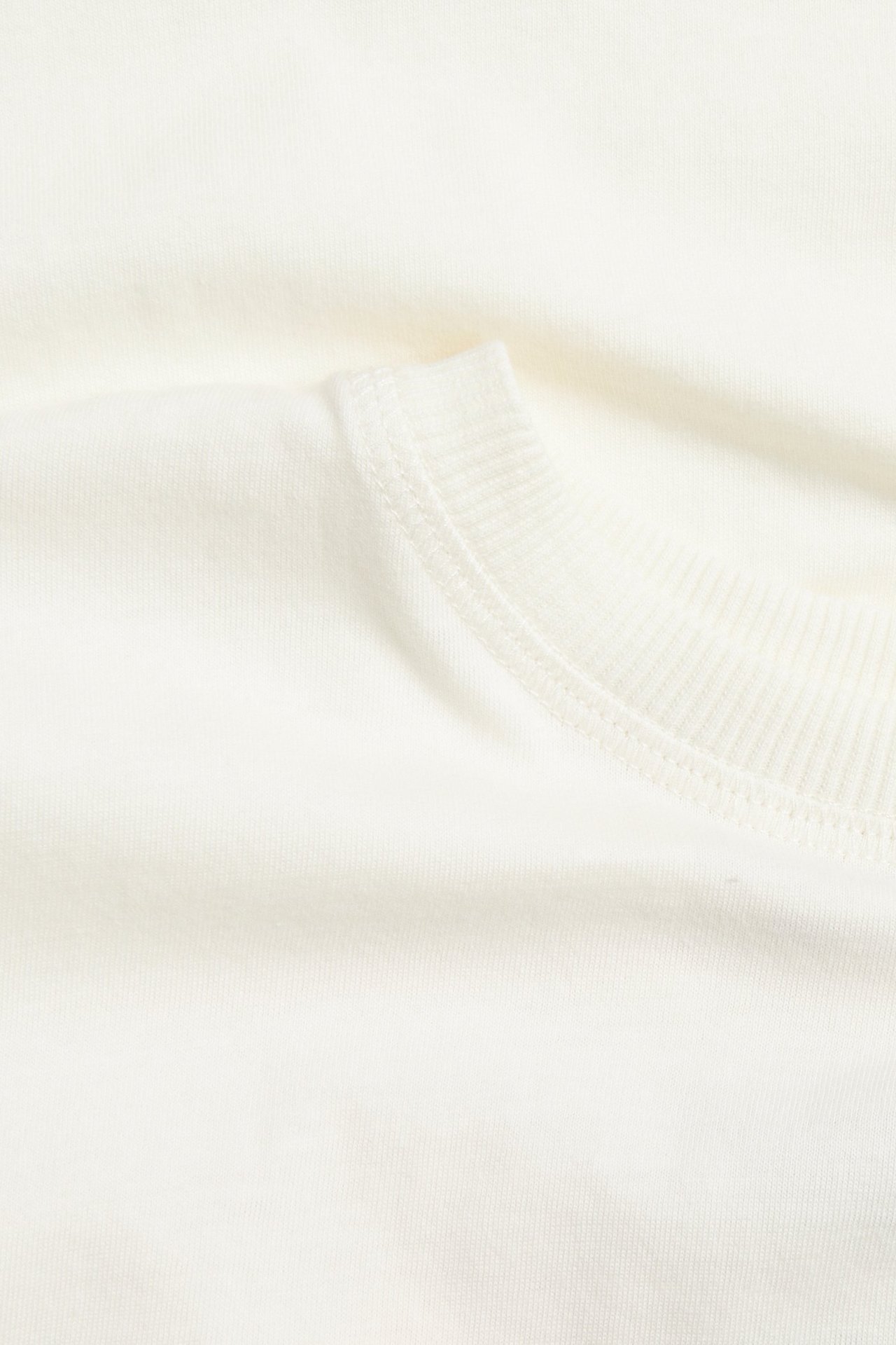 Närbild på en offwhite T-shirt i bomullsjersey med ribbad halsringning.