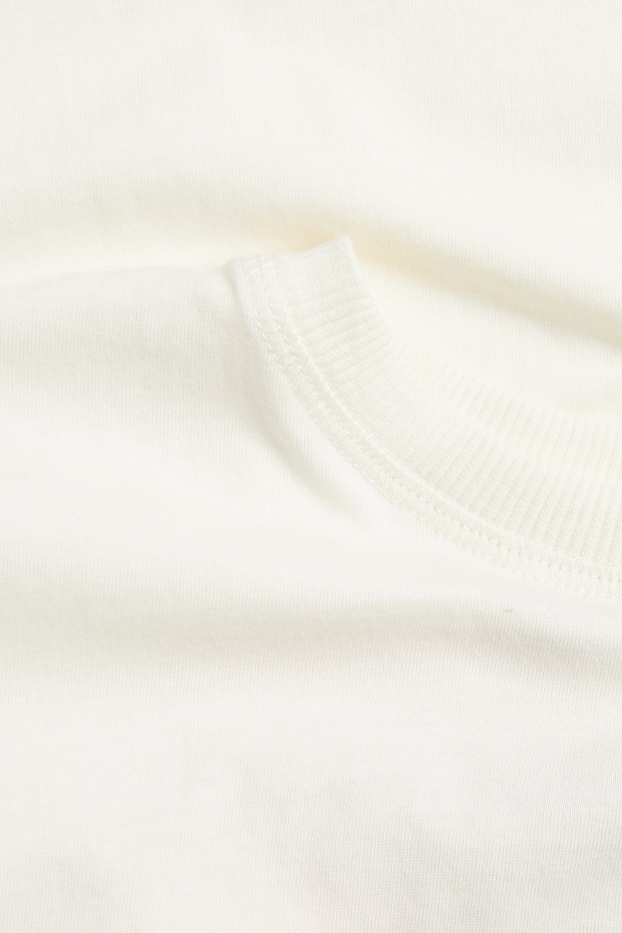 Lähikuva luonnonvalkoisesta puuvillatrikoisesta T-paidasta, jossa ribbineulottu pääntie.