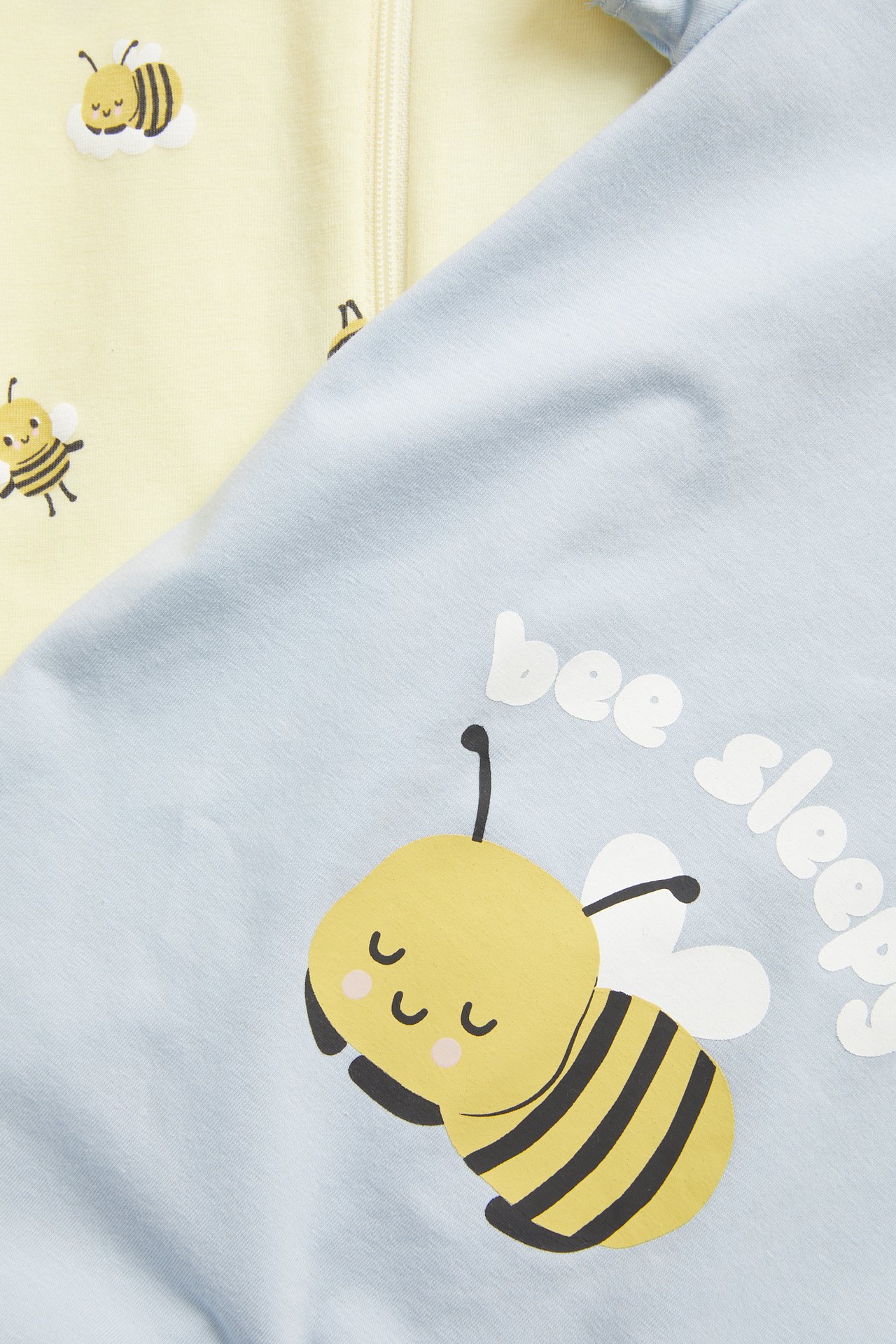 Närbild på en blå babyromper med sovande bi-tryck och en ljusgul romper med biomönster.