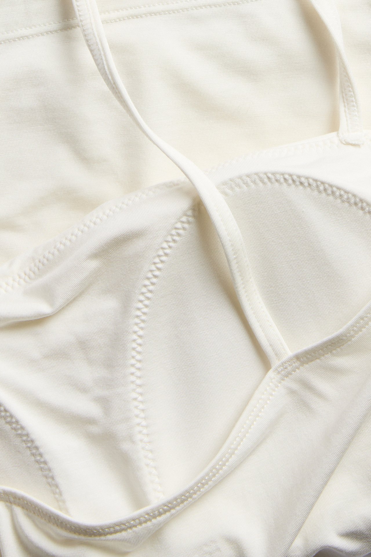 Zbliżenie na ecru singlet z lyocellu z wbudowanym biustonoszem, pokazujące szyte miseczki i cienki pasek.