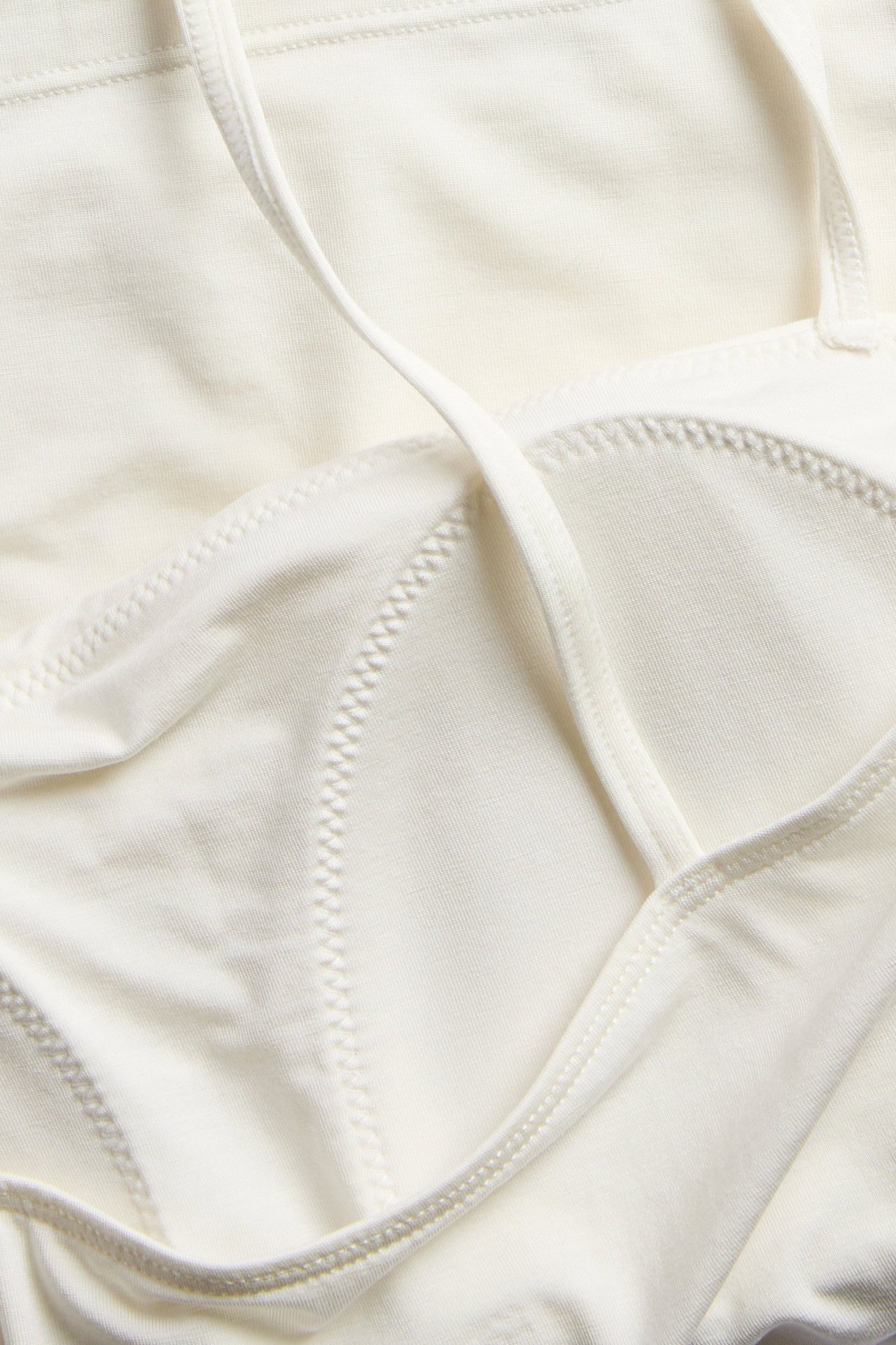Närbild av ett offwhite linne i lyocellmix med inbyggd bh, som visar sydda kupor och ett smalt axelband.