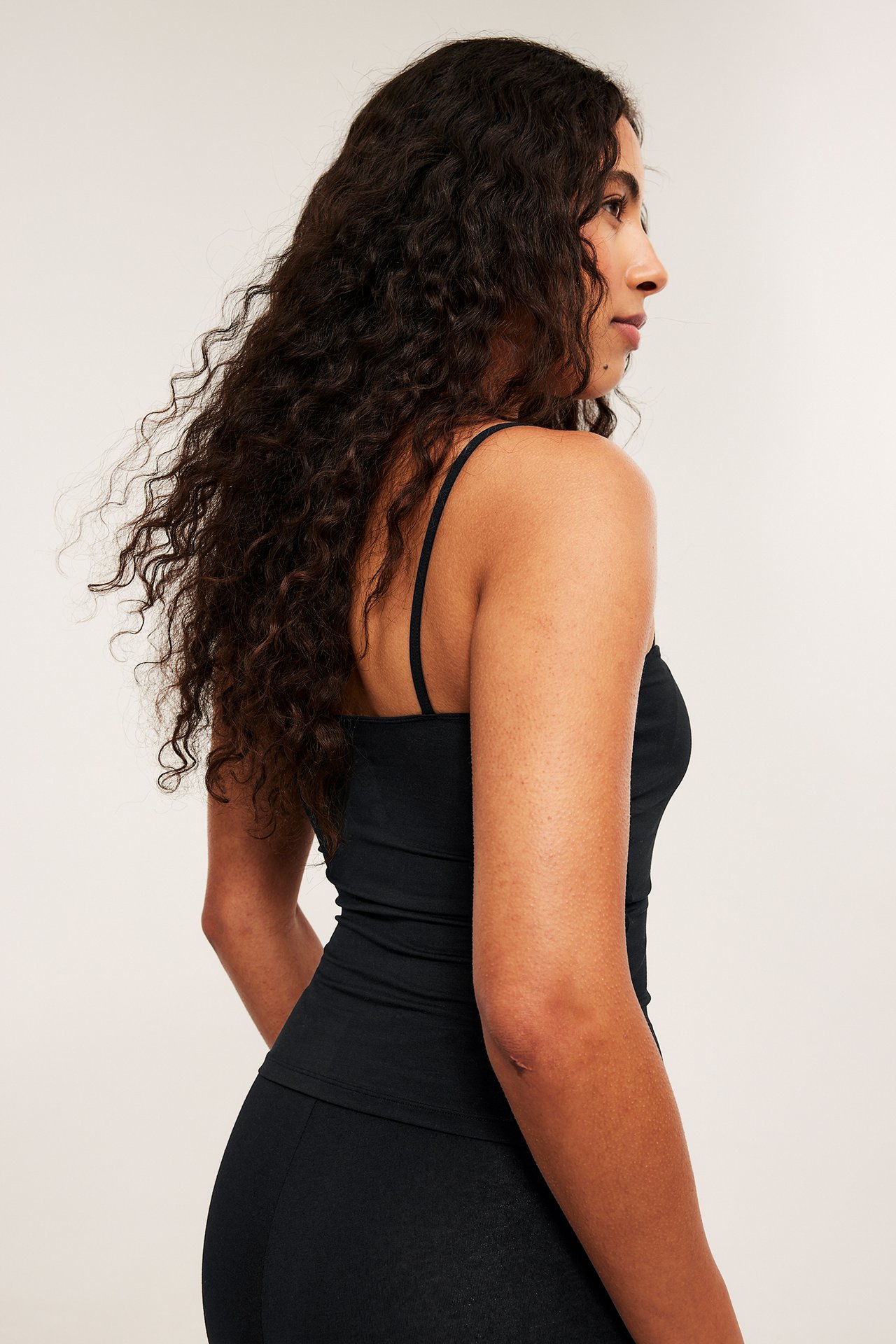 Widok z boku kobiety w dopasowanym czarnym topie z modalu na cienkich ramiączkach i legginsach.