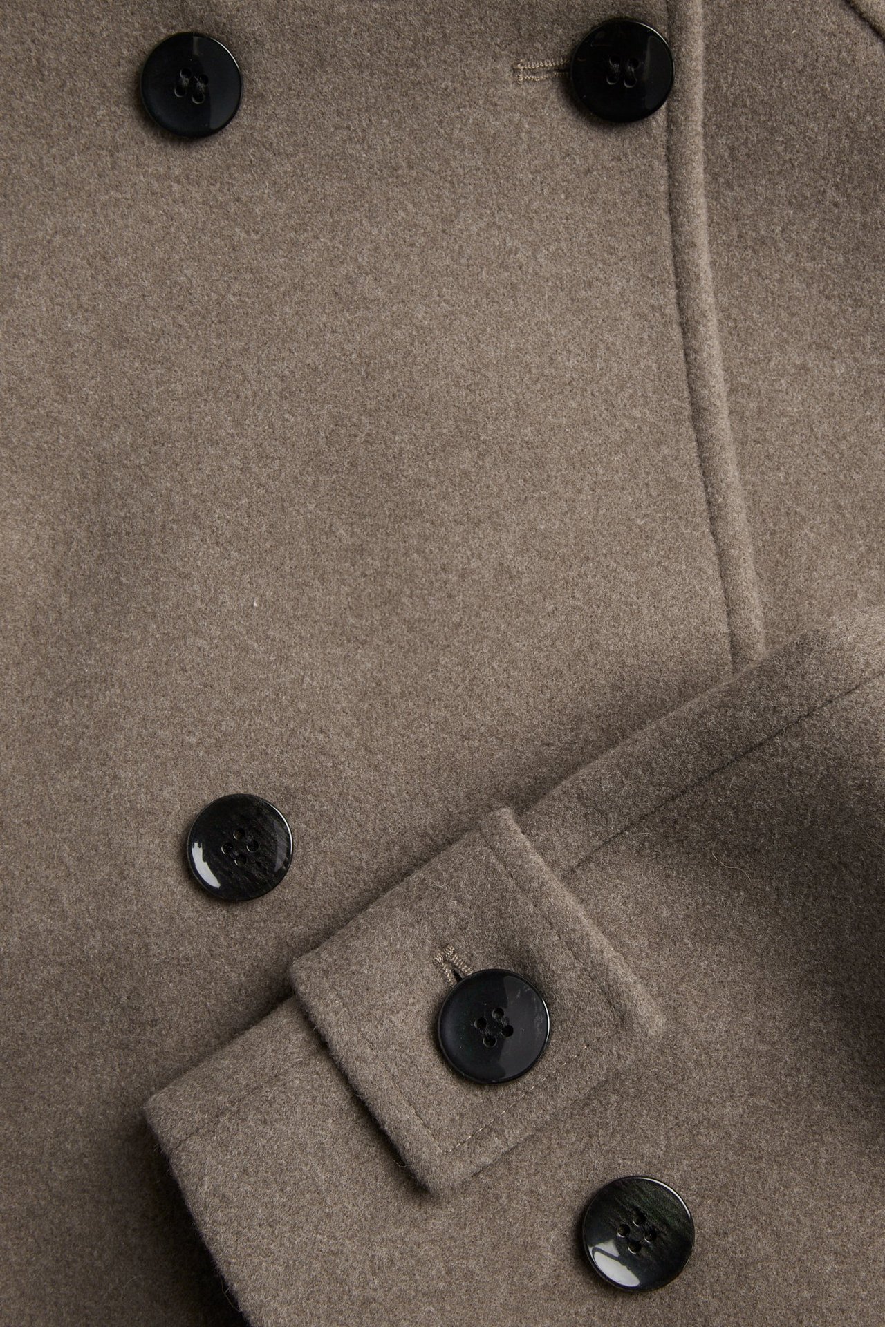 Zbliżenie brązowej melanżowej kurtki dwurzędowej z błyszczącymi czarnymi guzikami i detalem mankietu.