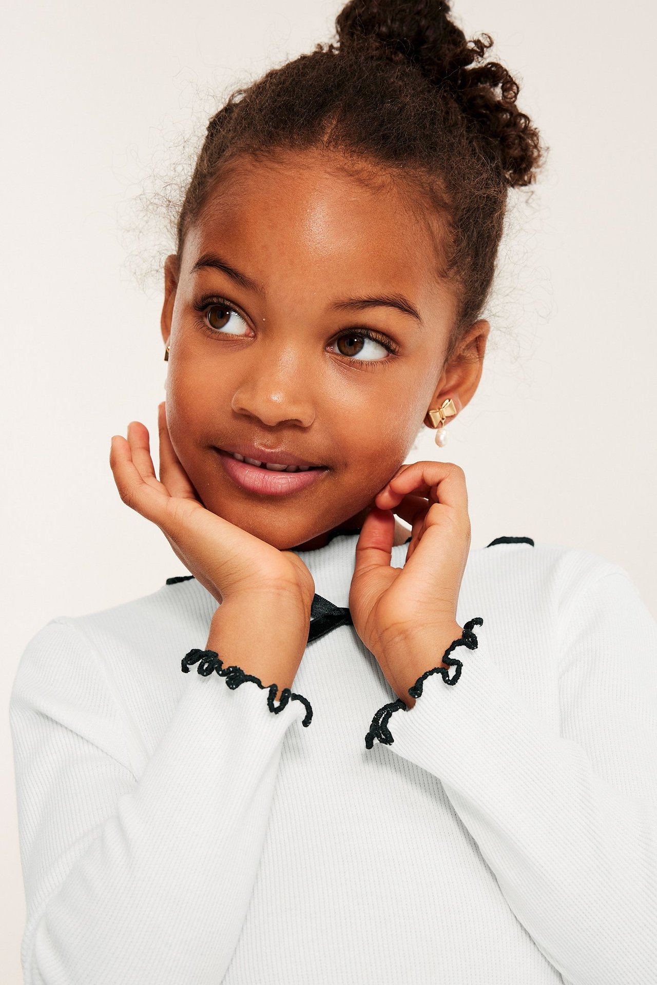 Barnkvinna i vit långärmad topp med svart rosett och ribbad bomull, frontvy.