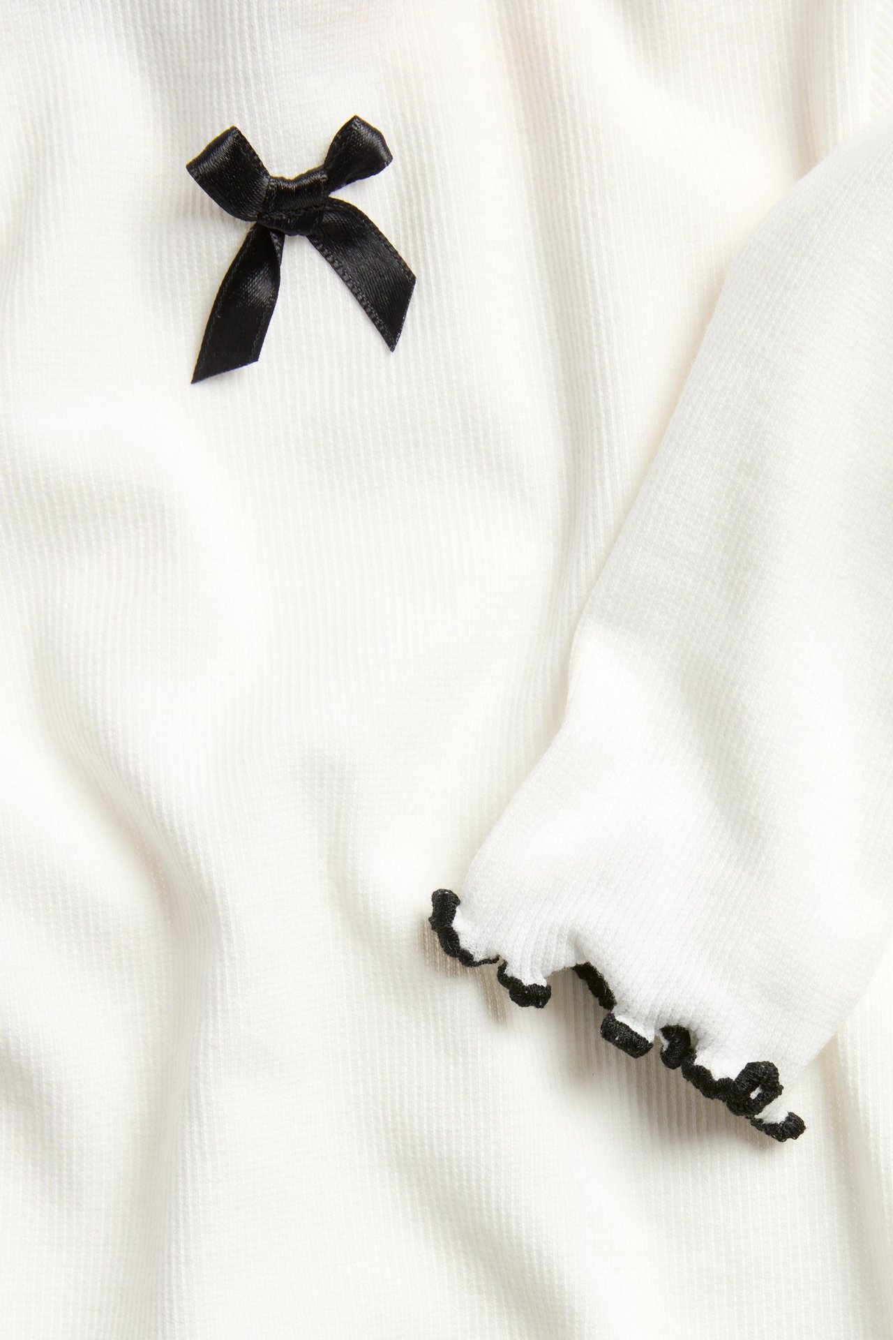 Długa biała koszulka dziecięca z czarną satynową kokardą i kontrastową lamówką.