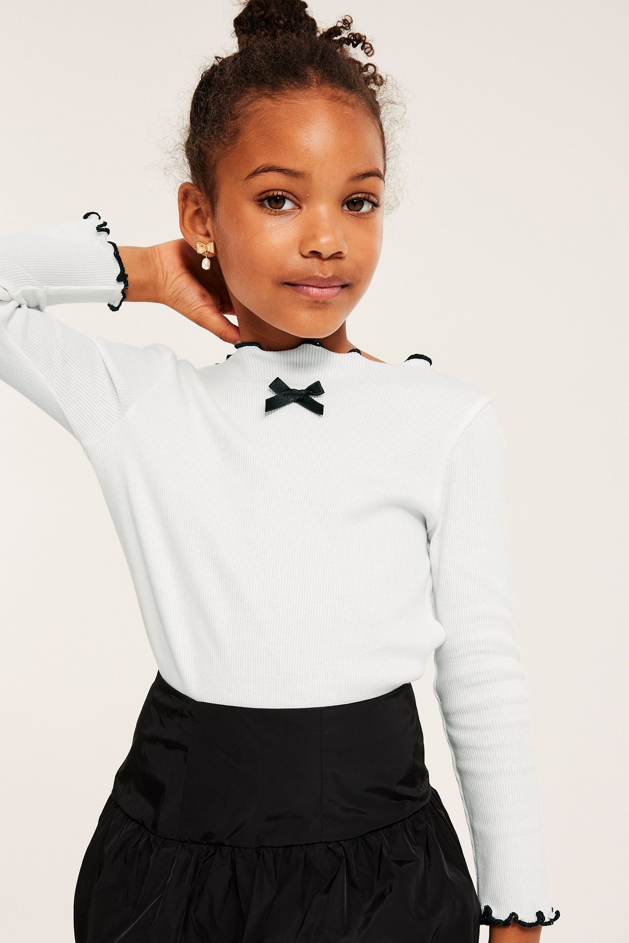 Vit långärmad trikåtopp med svart rosett framtill, ribbad bomull, kontrastfärgad babylock.