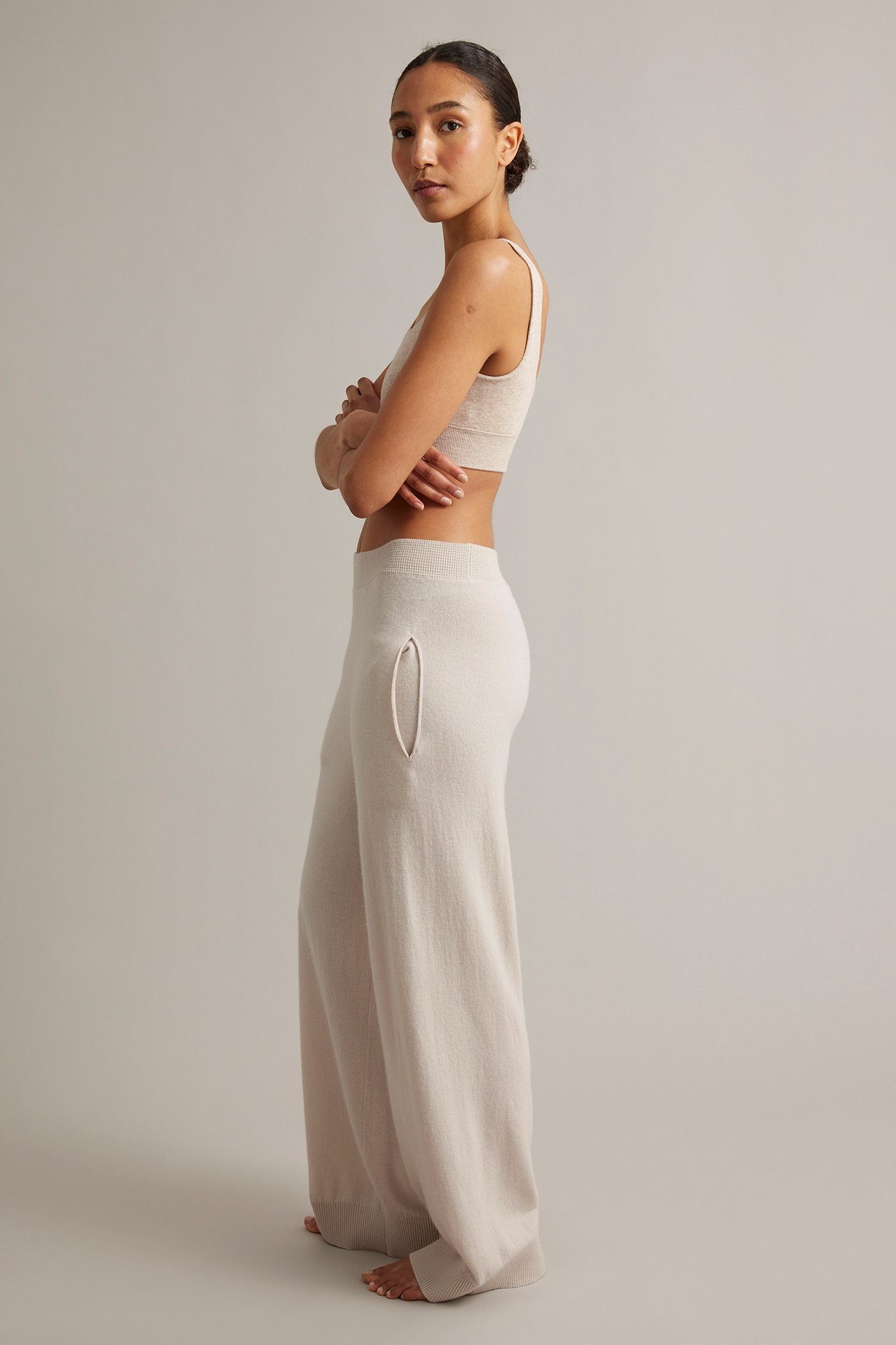 Naisen sivukuva: vaaleanbeiget neulotut villacashmerehousut taskuilla ja yhteensopiva toppi.