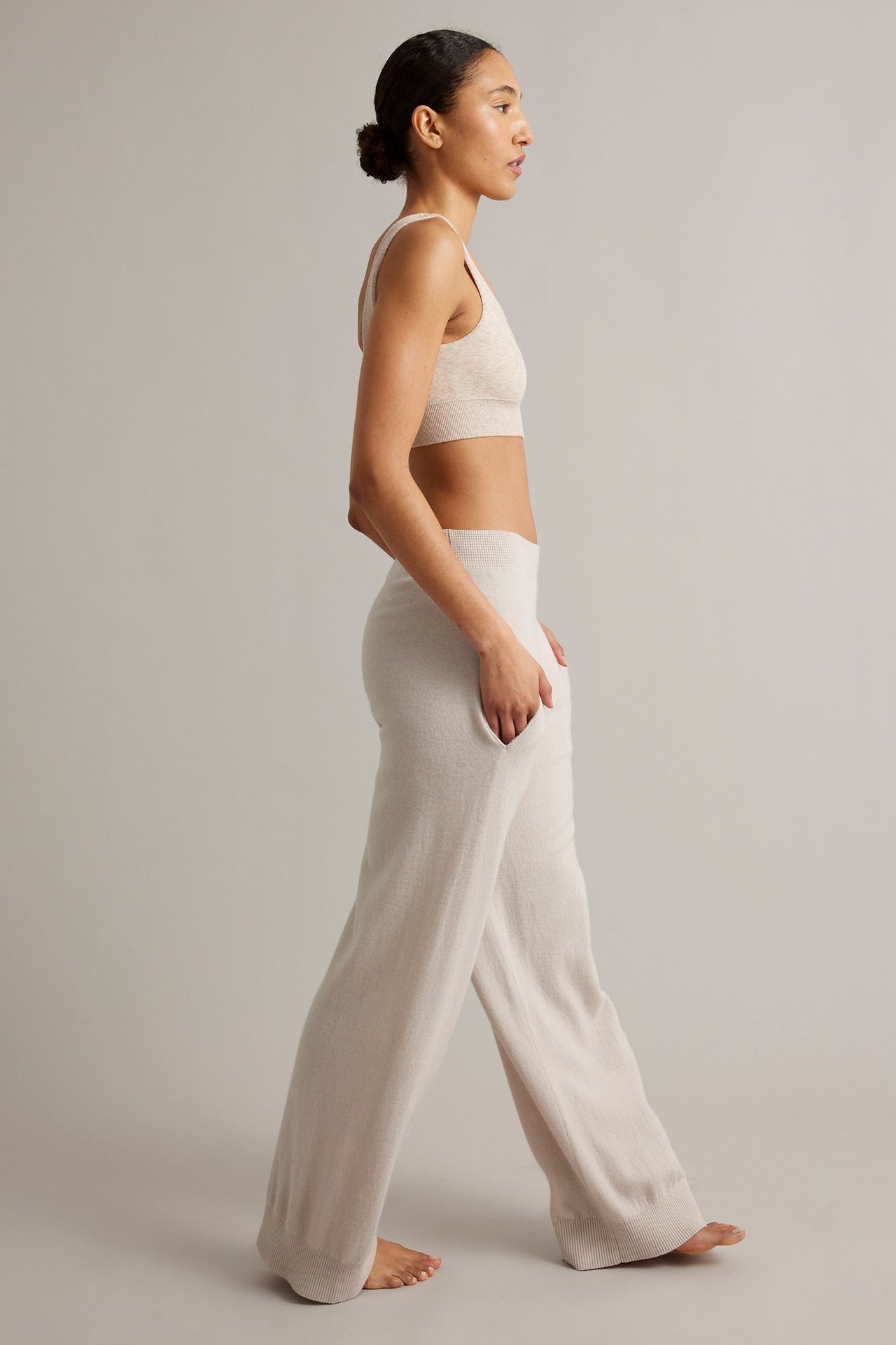 Naisen sivukuva yllään vaaleabeiget neulotut leveälahkeiset housut taskuilla ja yhteensopiva rintaliivitoppi.