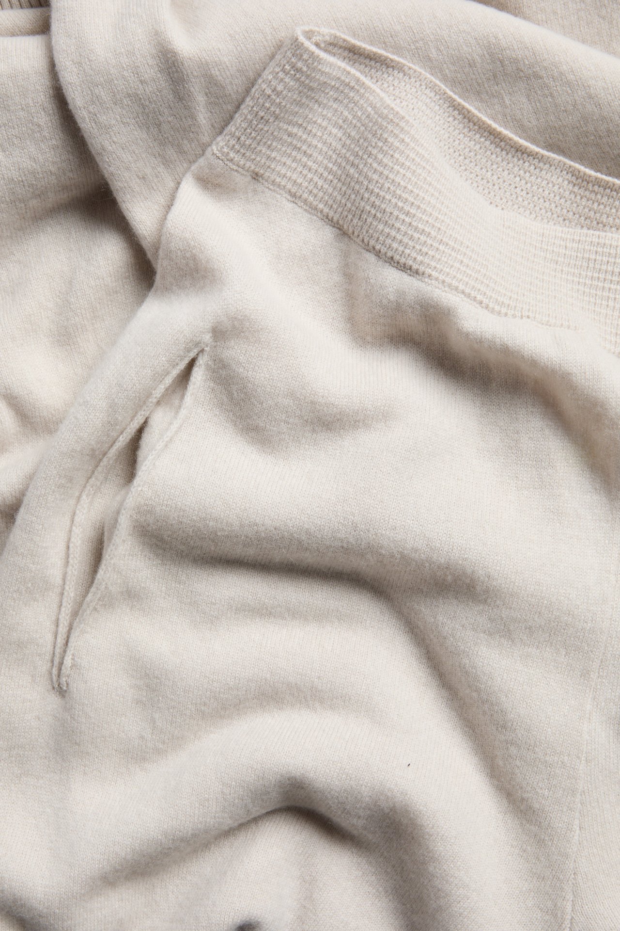 Närbild av ljusbeige stickade byxor i ull- och kashmirmix med sidoficka och ribbstickad detalj.