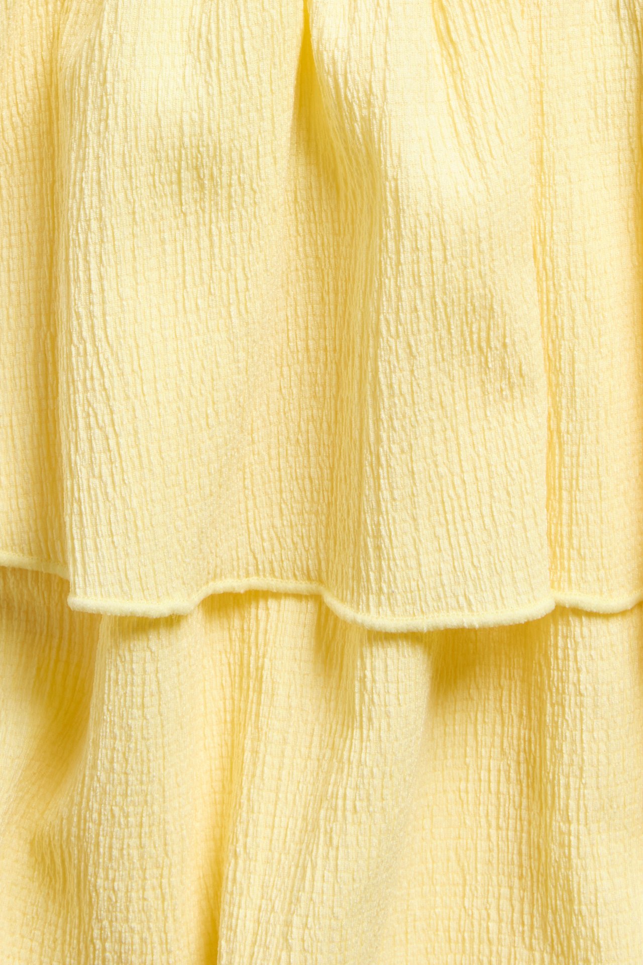 Närbild på en ljusgul kort volangkjol i krinklad jersey med två synliga volanger.