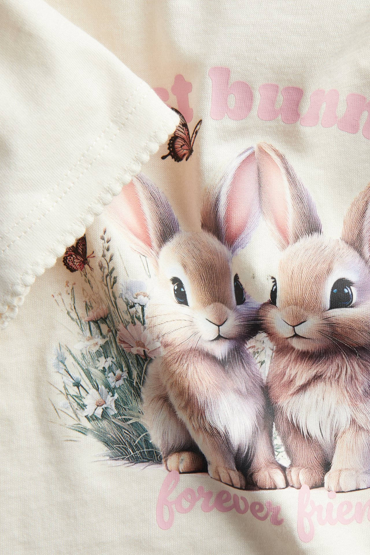 Närbild framifrån av offwhite barntröja i bomull med kanintryck och picotsömmar.