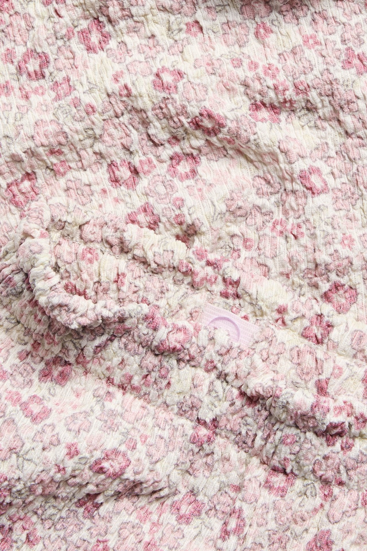 Zbliżenie na écru kwieciste kuloty: strukturalna dzianina, różowy wzór, elastyczna falbaniasta talia, wewnętrzny regulowany guzik.