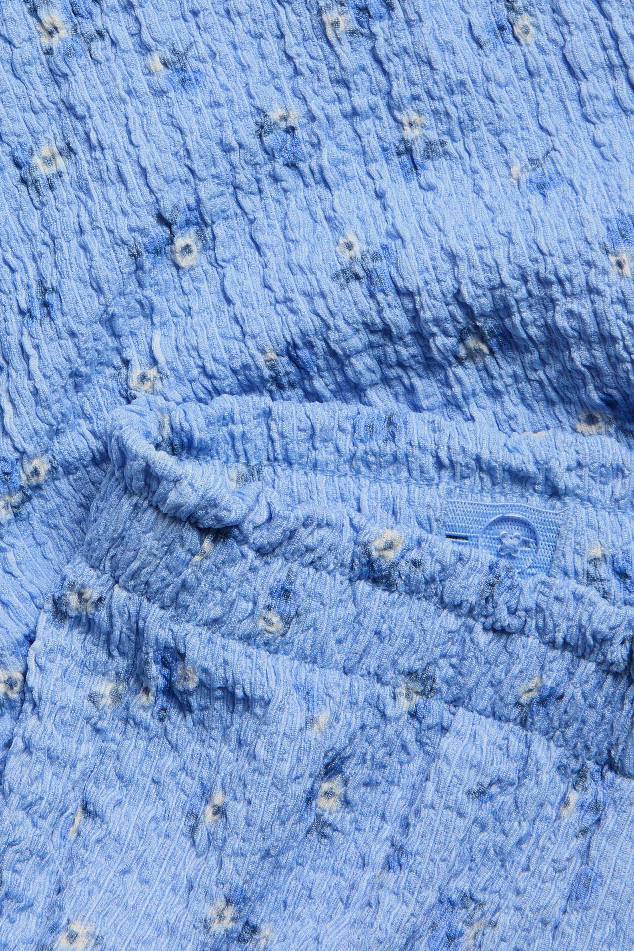 Zbliżenie: jasnoniebieskie kuloty w kwiaty, strukturalna dzianina, elastyczny pas z falbanką, guzik.