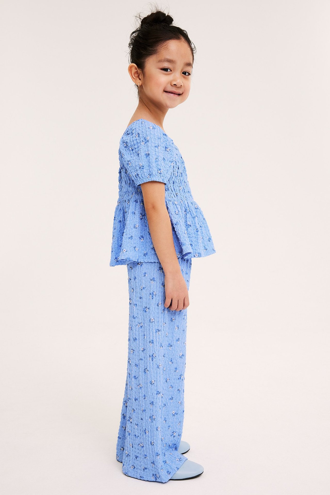 Widok z boku dziecka w jasnoniebieskich kwiecistych kulotach i pasującym marszczonym topie.