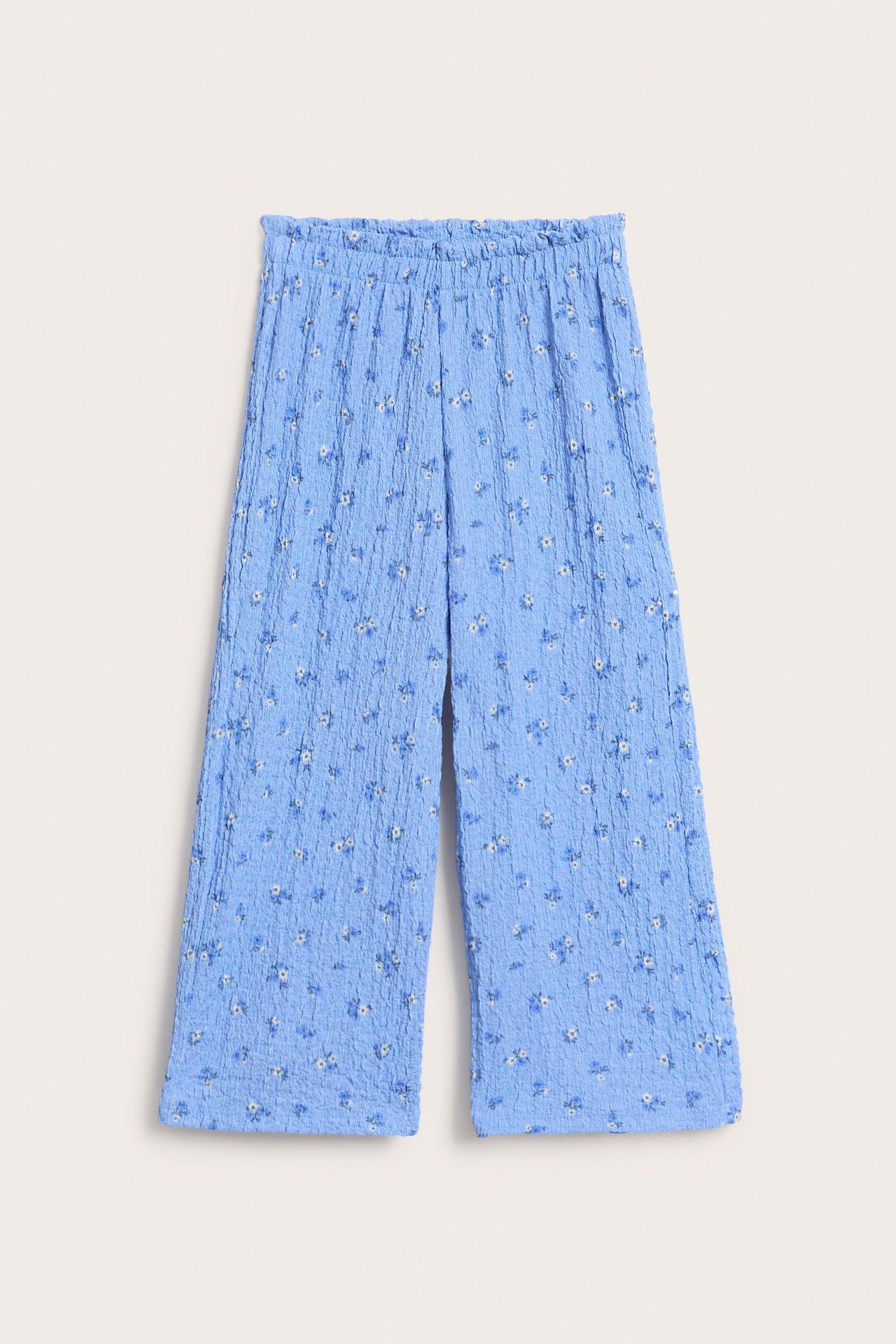 Widok z przodu jasnoniebieskich teksturowanych kulotów z szerokimi nogawkami, elastyczną falbanką w talii i kwiatowym wzorem.