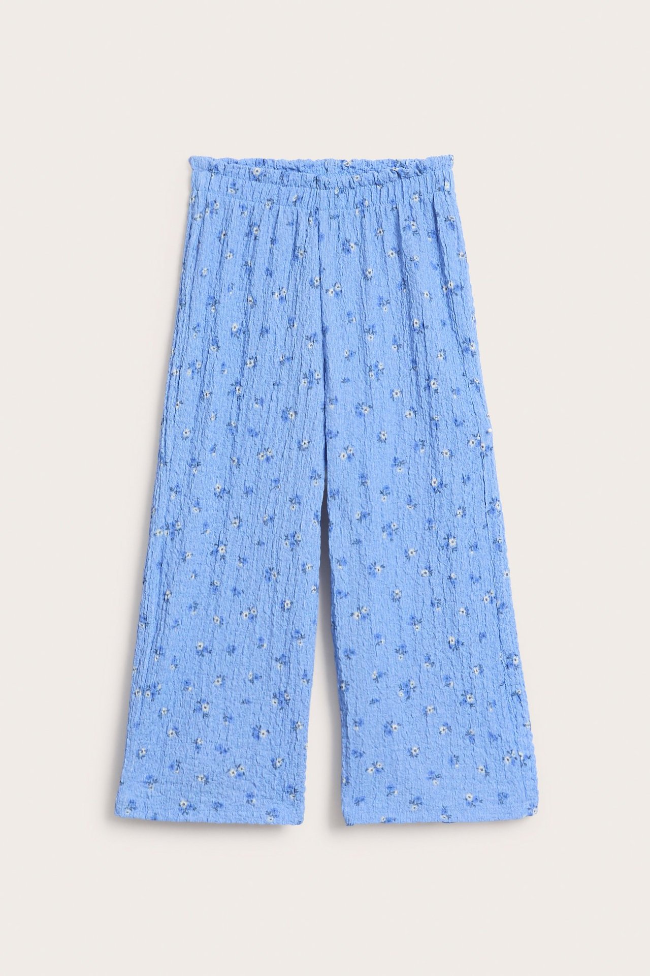 Widok z przodu jasnoniebieskich teksturowanych kulotów z szerokimi nogawkami, elastyczną falbanką w talii i kwiatowym wzorem.