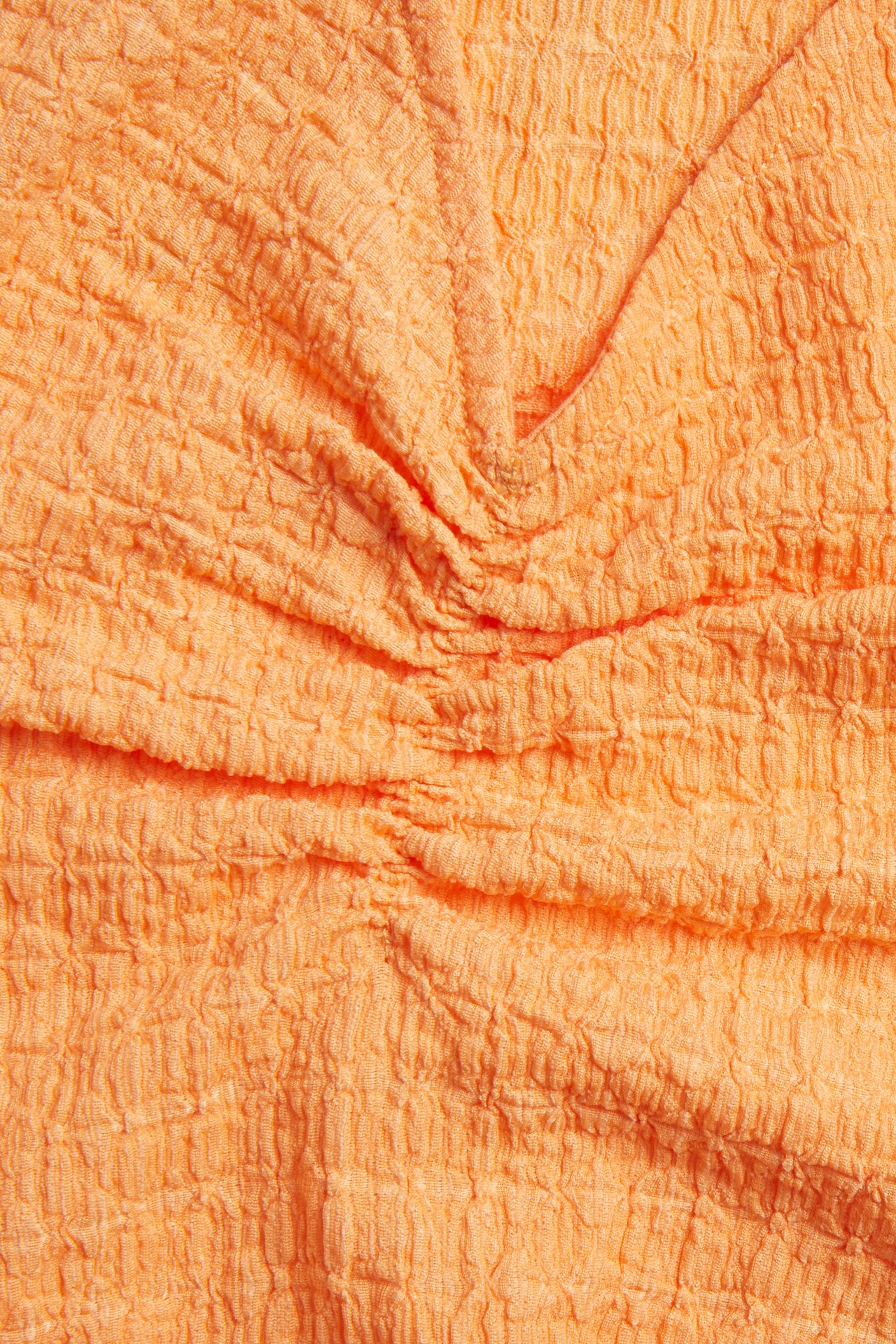 Närbild av en orange strukturerad topp i polyesterblandning med krinklad textur.