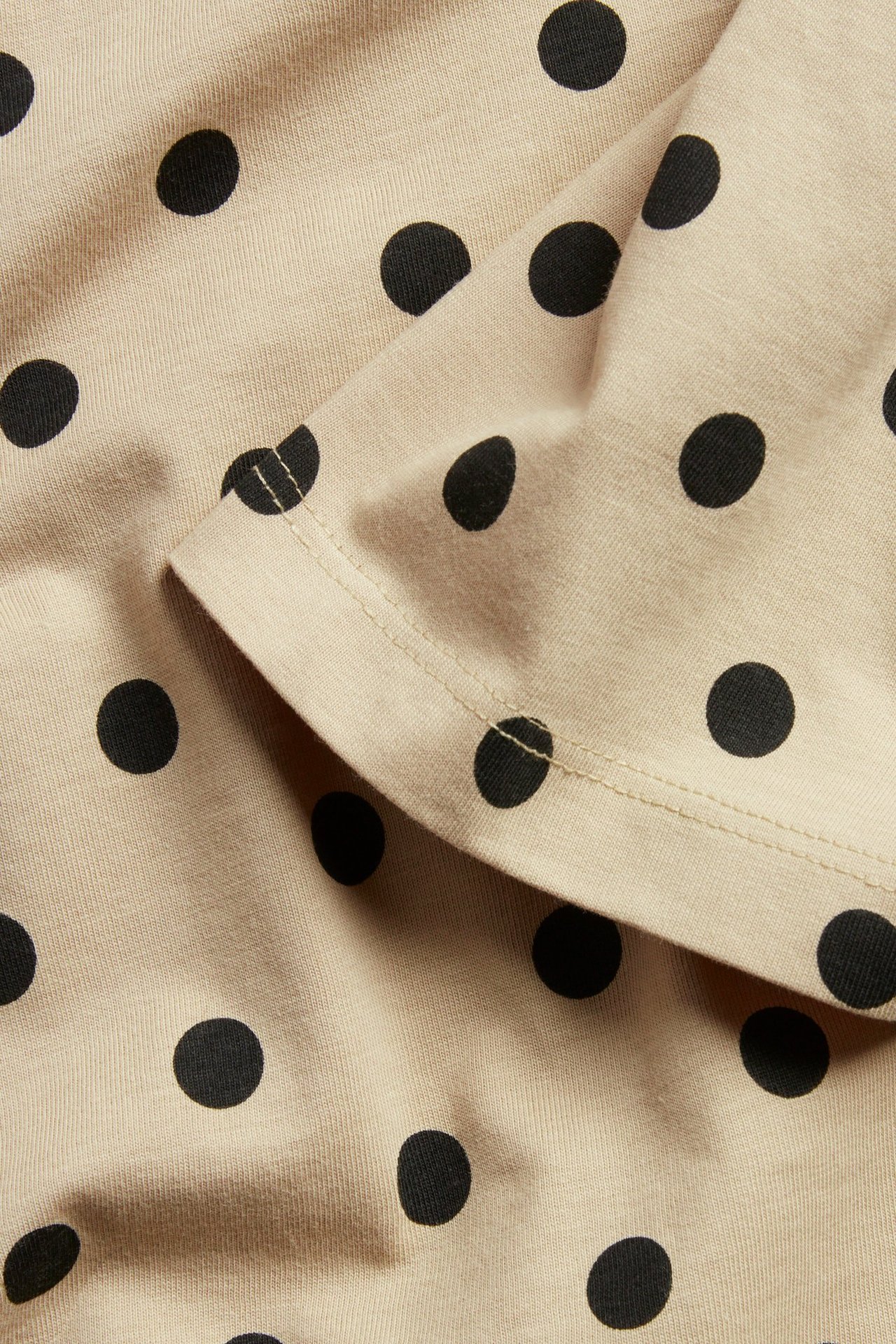 Zbliżenie beżowej bawełnianej tuniki-koszulki w czarne kropki, pokazujące starannie obszyty złożony brzeg.