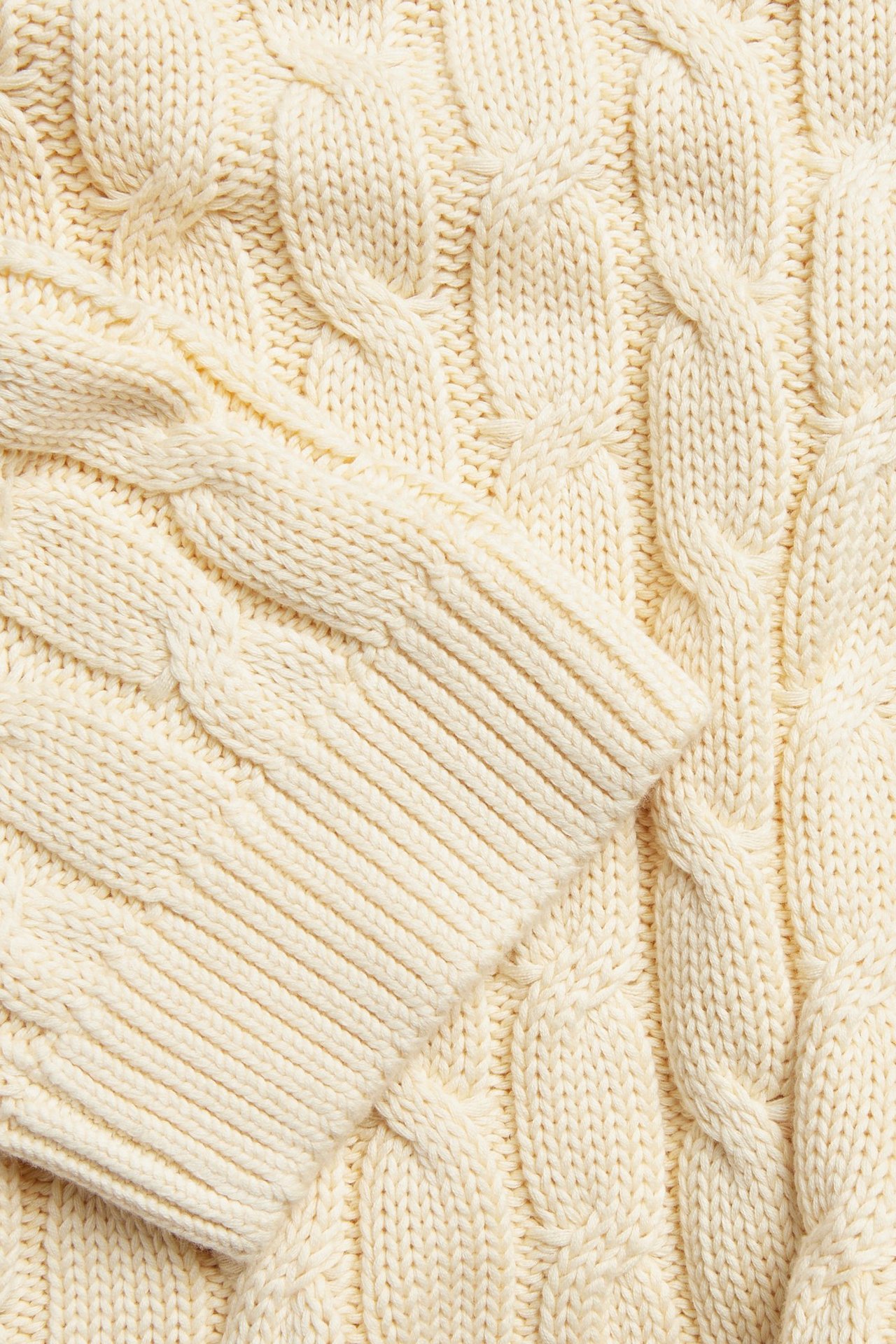 Nærbilde av en lys gul kabelstrikket bomullsgenser med en ribbestrikket mansjett.