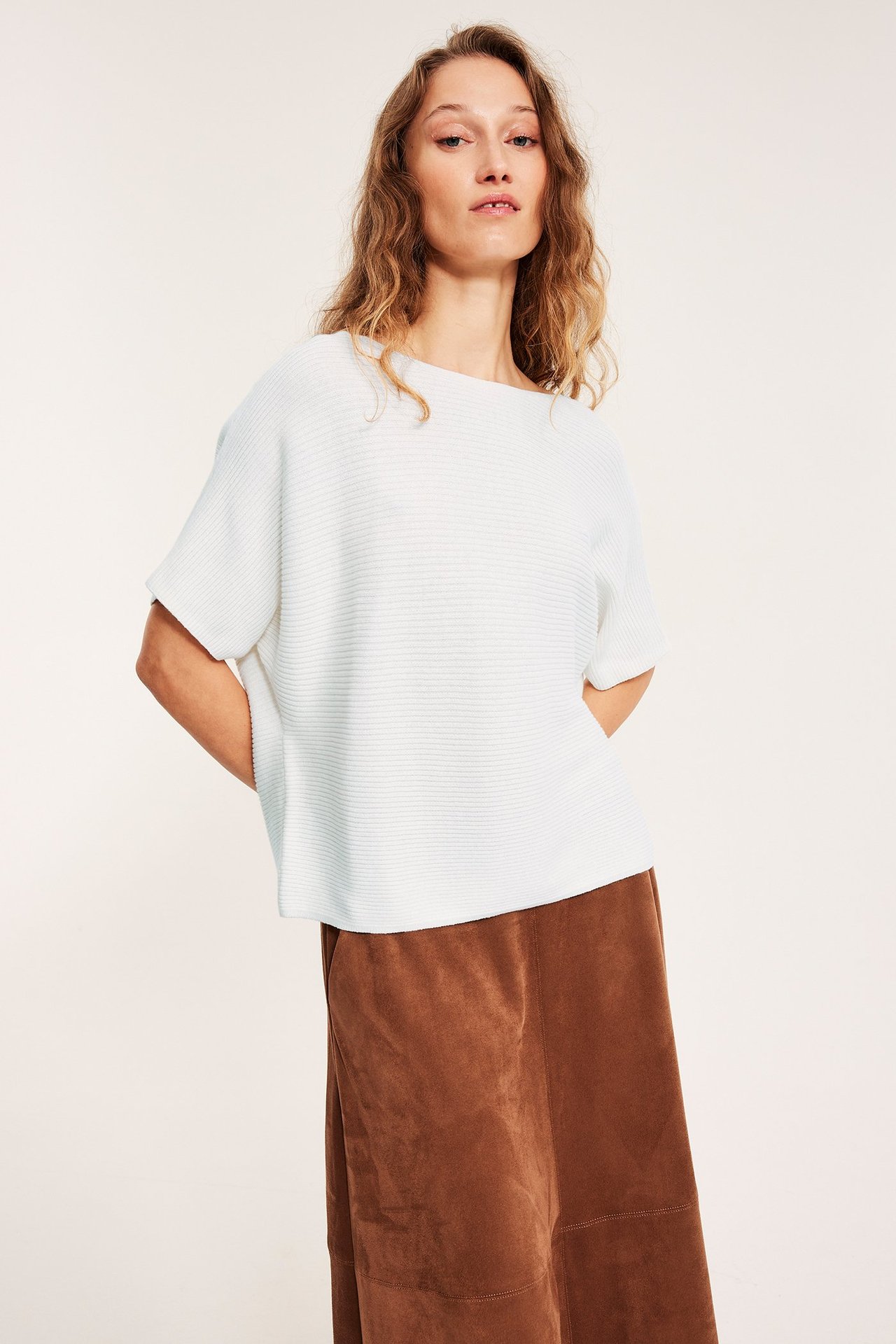 Front: kvinne i hvit ribbestrikket kortarmet bomullsgenser og brunt semsket skjørt.