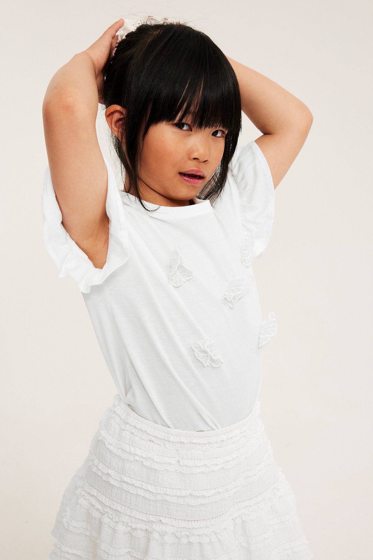 Barnets offwhite T-skjorte med volangermer, sommerfuglapplikasjoner og et hvitt lagsdelt skjørt.