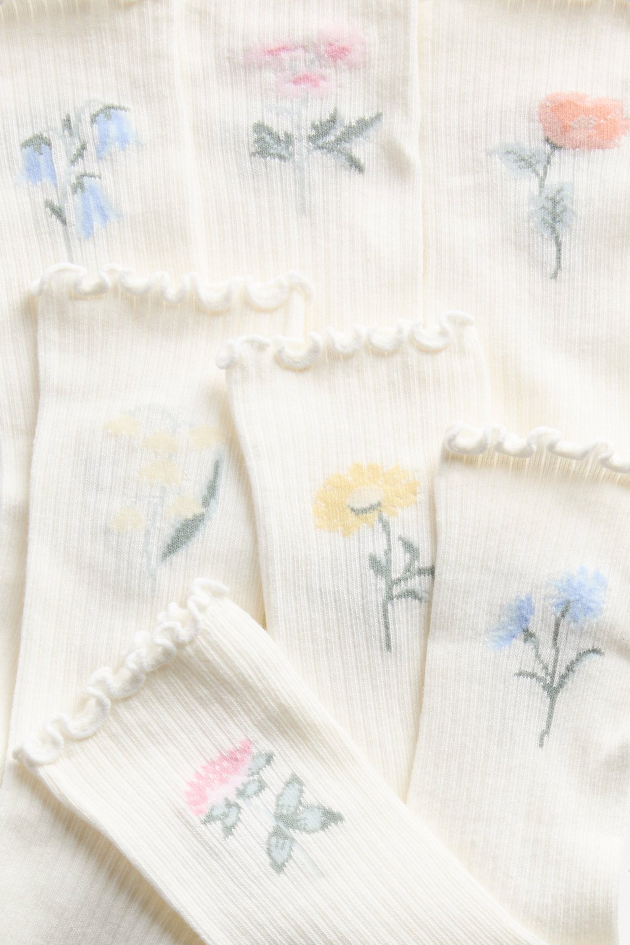 Lähikuva luonnonvalkoisista ribatuista sukista, joissa on röyhelöreunat ja kirjaillut kukkia.