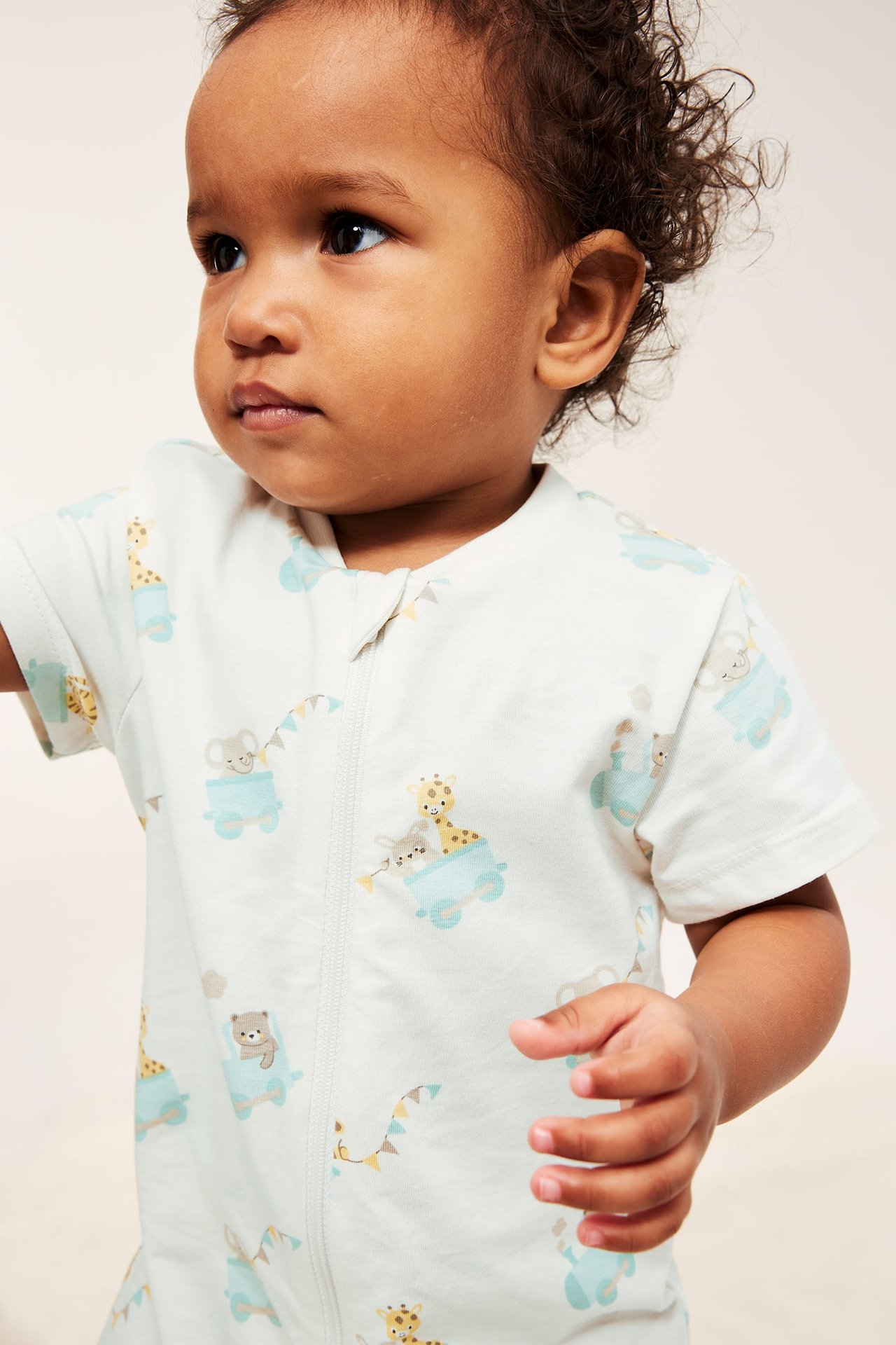 Närbild på en baby i en offwhite kortärmad romper med djurmönster och tvåvägsdragkedja.