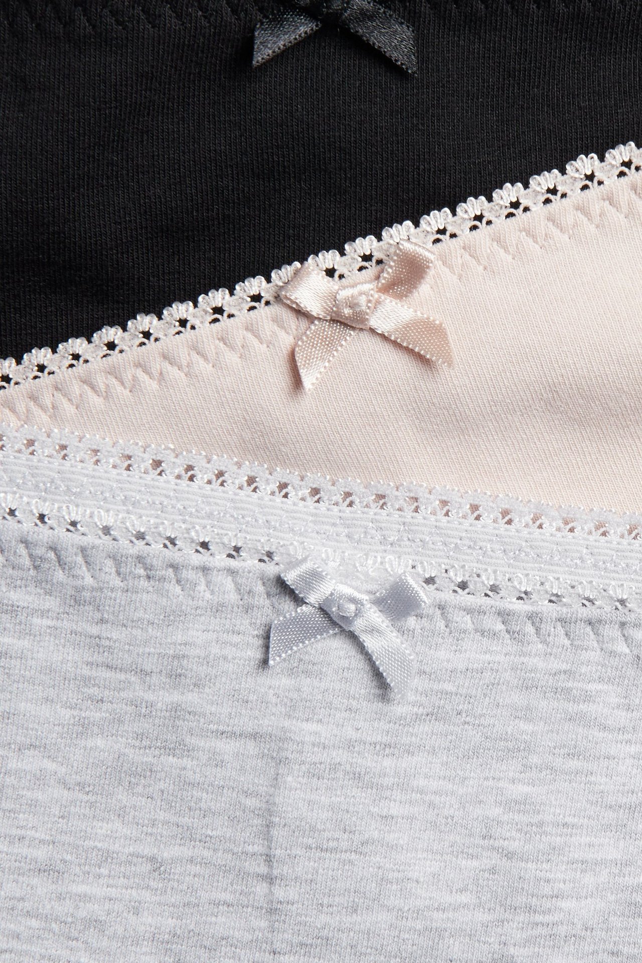 Nærbilde av tre bomullsboxere: svarte, lys rosa og grå, med picotkanter og sløyfer.