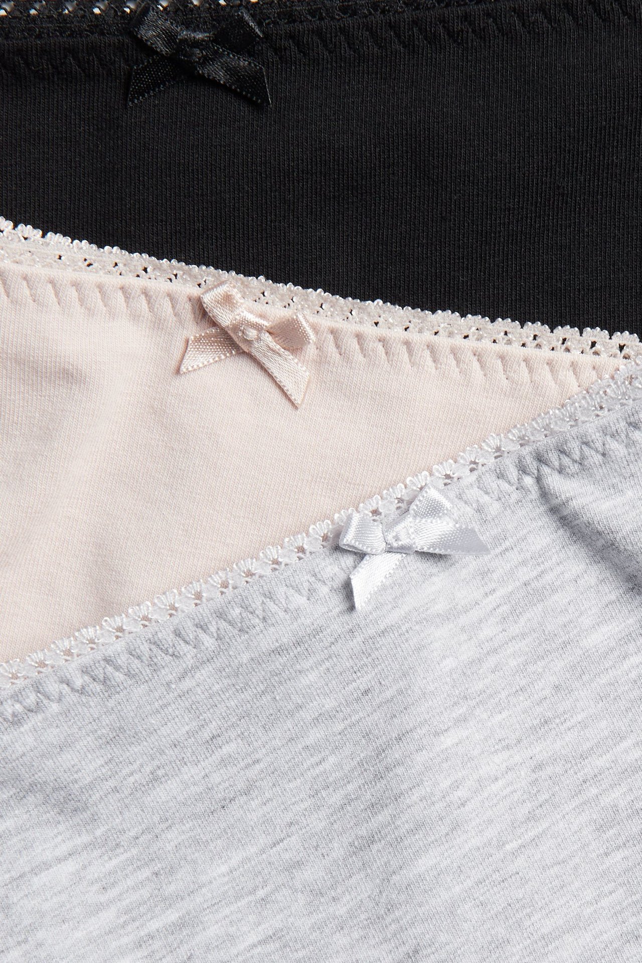 Nærbilde av tre bomullstruser i svart, lys rosa og lys grå, med picotkant og liten sløyfe.