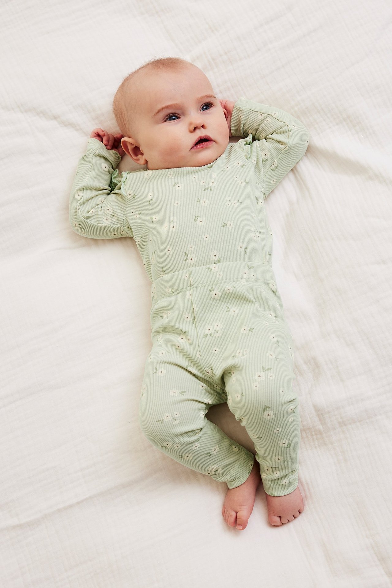 Ylhäältä näkymä: vauva, yllään vaaleanvihreä ribattu body valkoisella kukkakuviolla, röyhelöillä, ja leggingsit.