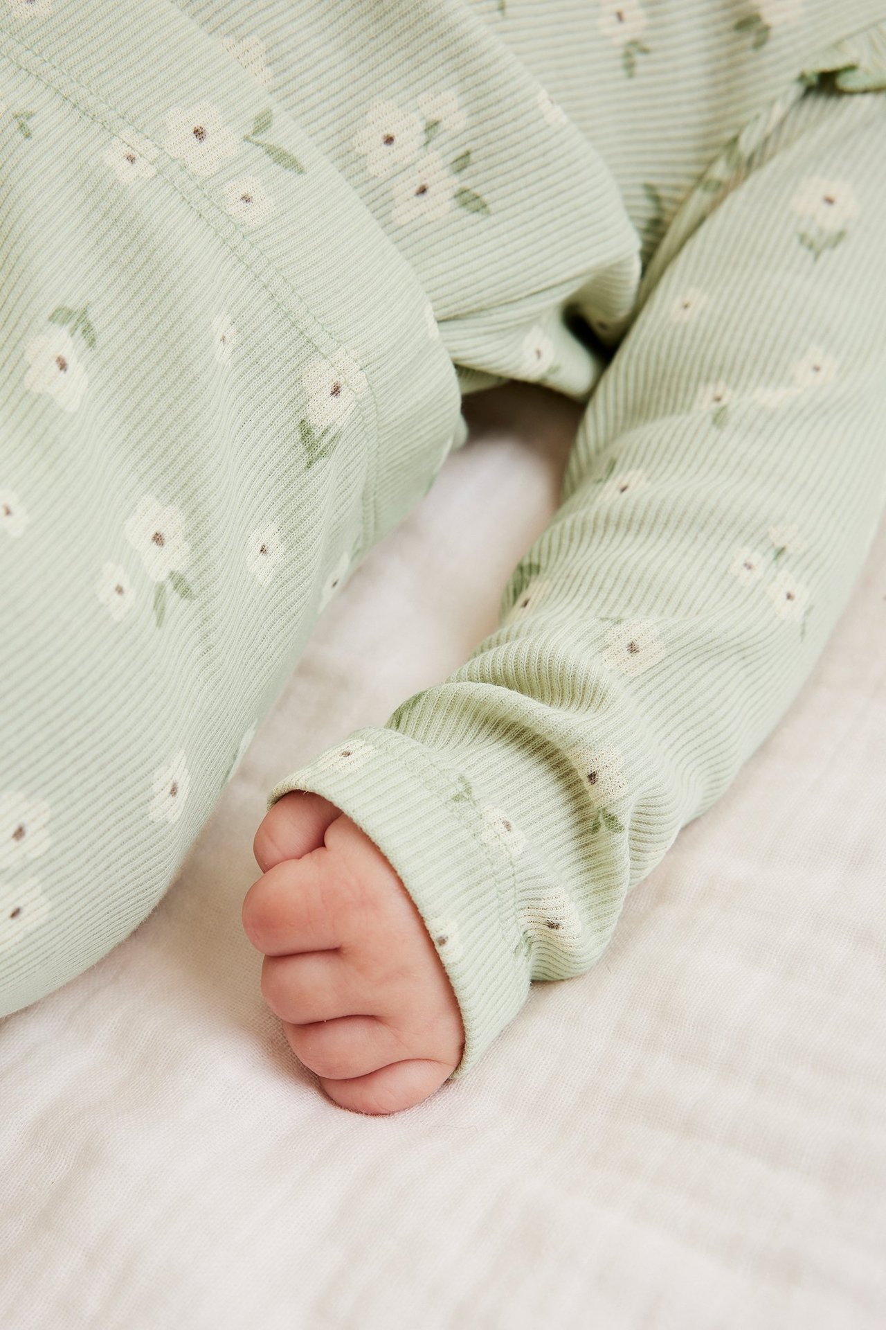 Lähikuva vauvasta yllään vaaleanvihreä ribattu kukkakuvioinen body olkafrillalla.