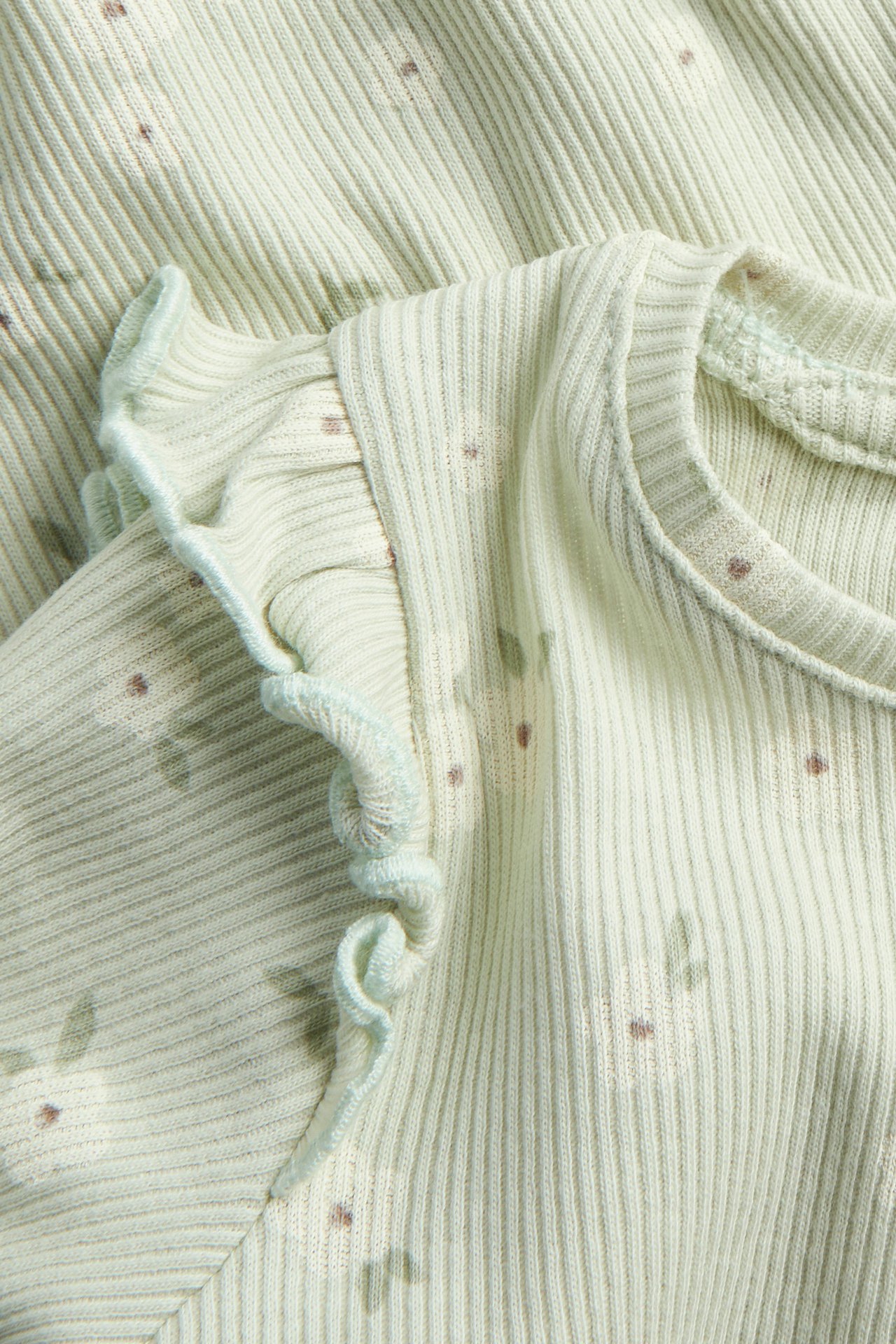 Zbliżenie na jasnozielone prążkowane body niemowlęce z falbanką na ramieniu i kwiecistym wzorem.