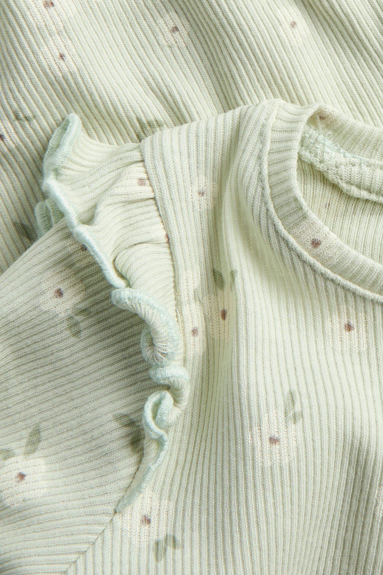 Zbliżenie na jasnozielone prążkowane body niemowlęce z falbanką na ramieniu i kwiecistym wzorem.