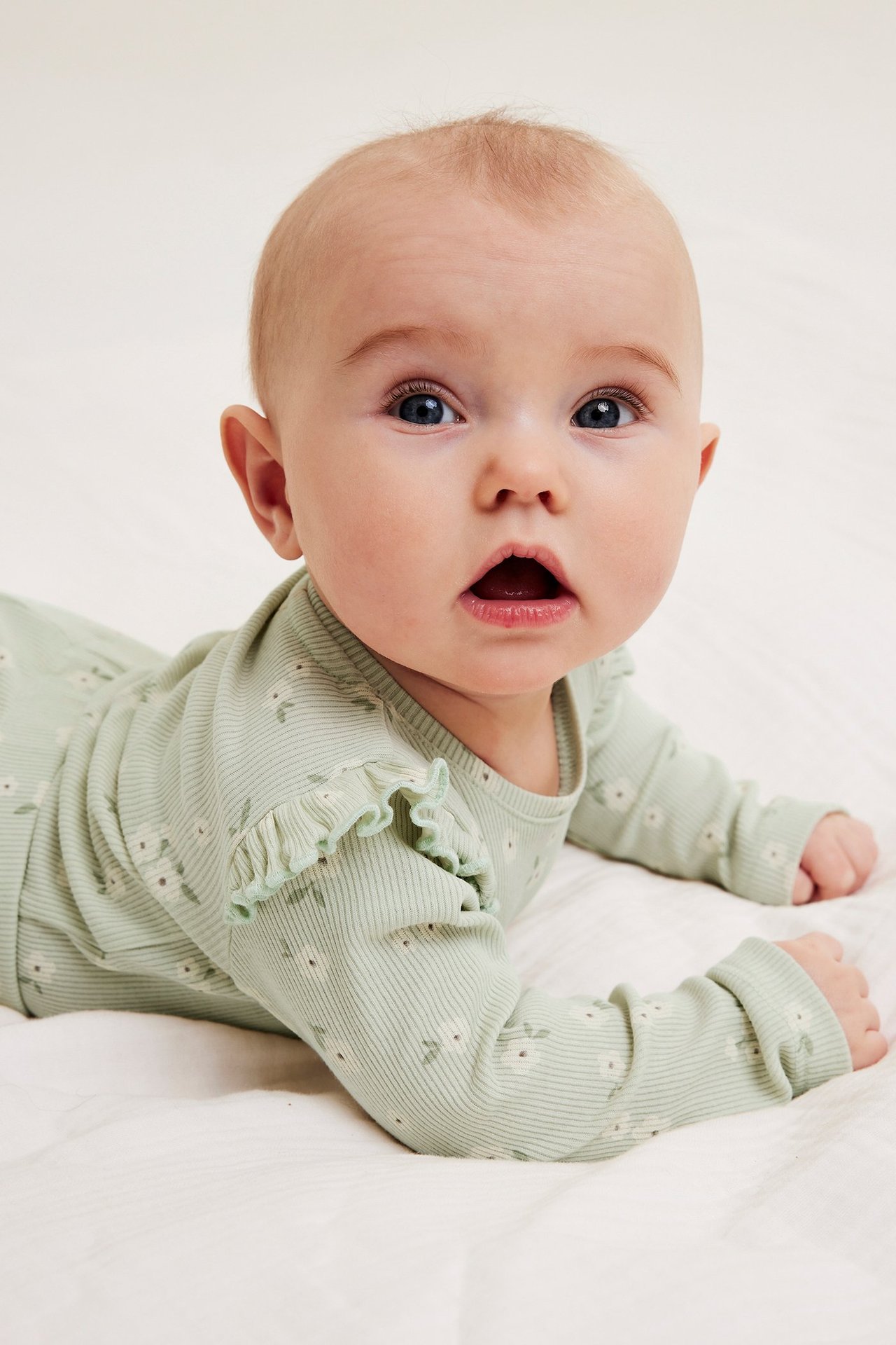 Widok z przodu na dziecko w jasnozielonym prążkowanym body w kwiaty z falbankami.