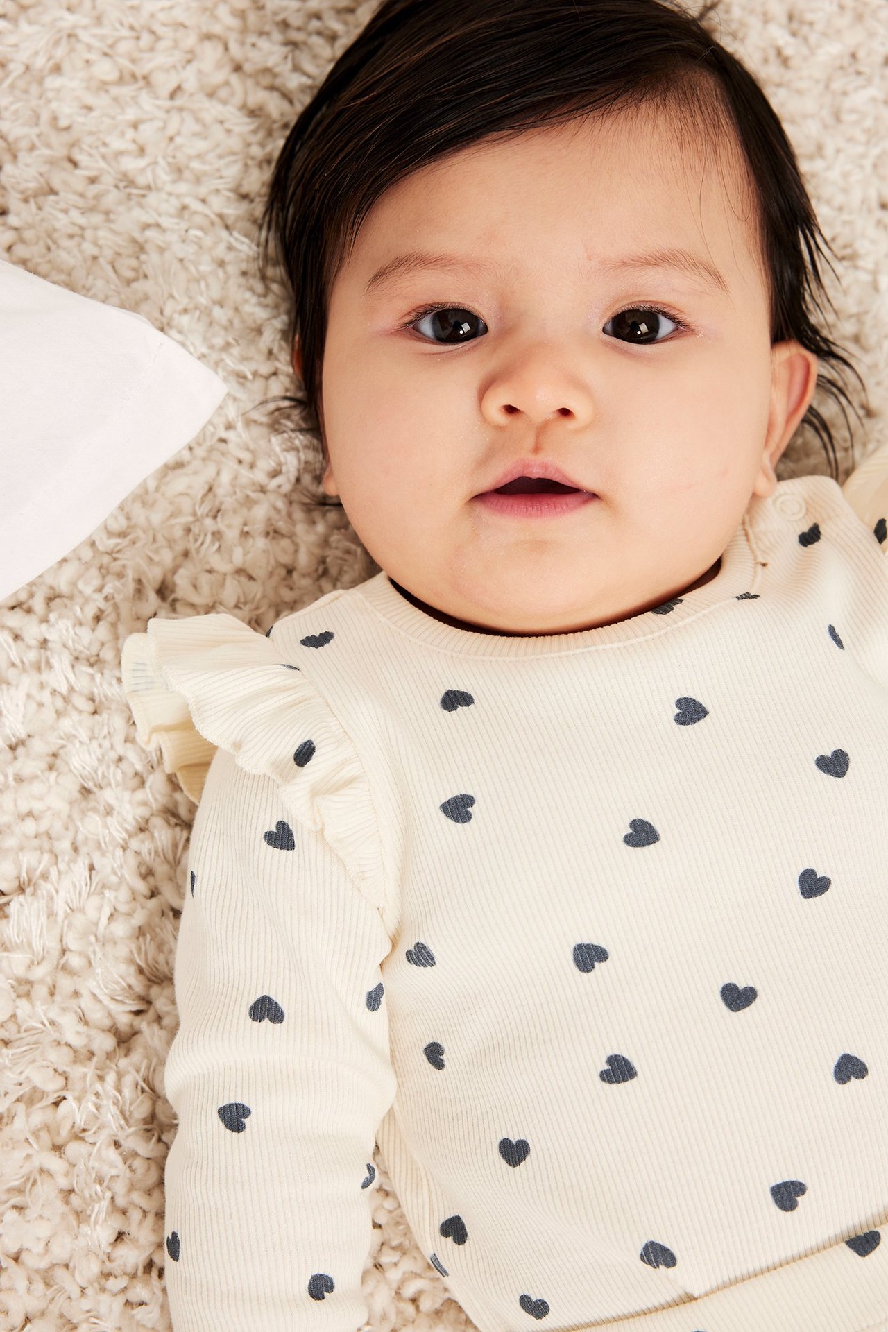 Lähikuva vauvasta, yllään luonnonvalkoinen ribattu body tummalla sydänkuviolla ja olkarypytyksillä.