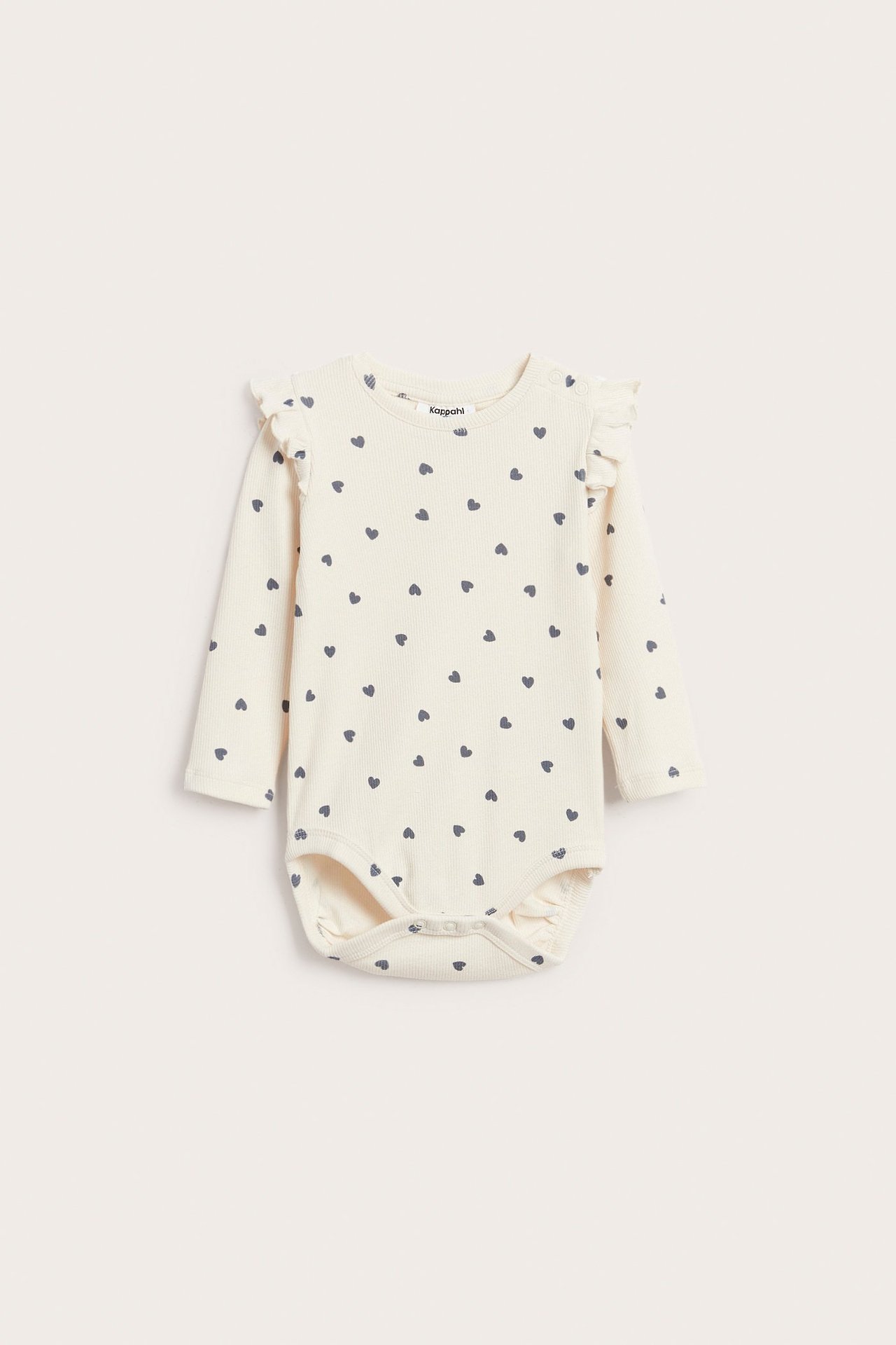 Edestä kuvattu luonnonvalkoinen ribattu vauvan body röyhelöillä, kauttaaltaan tummalla sydänkuviolla ja painonapeilla.