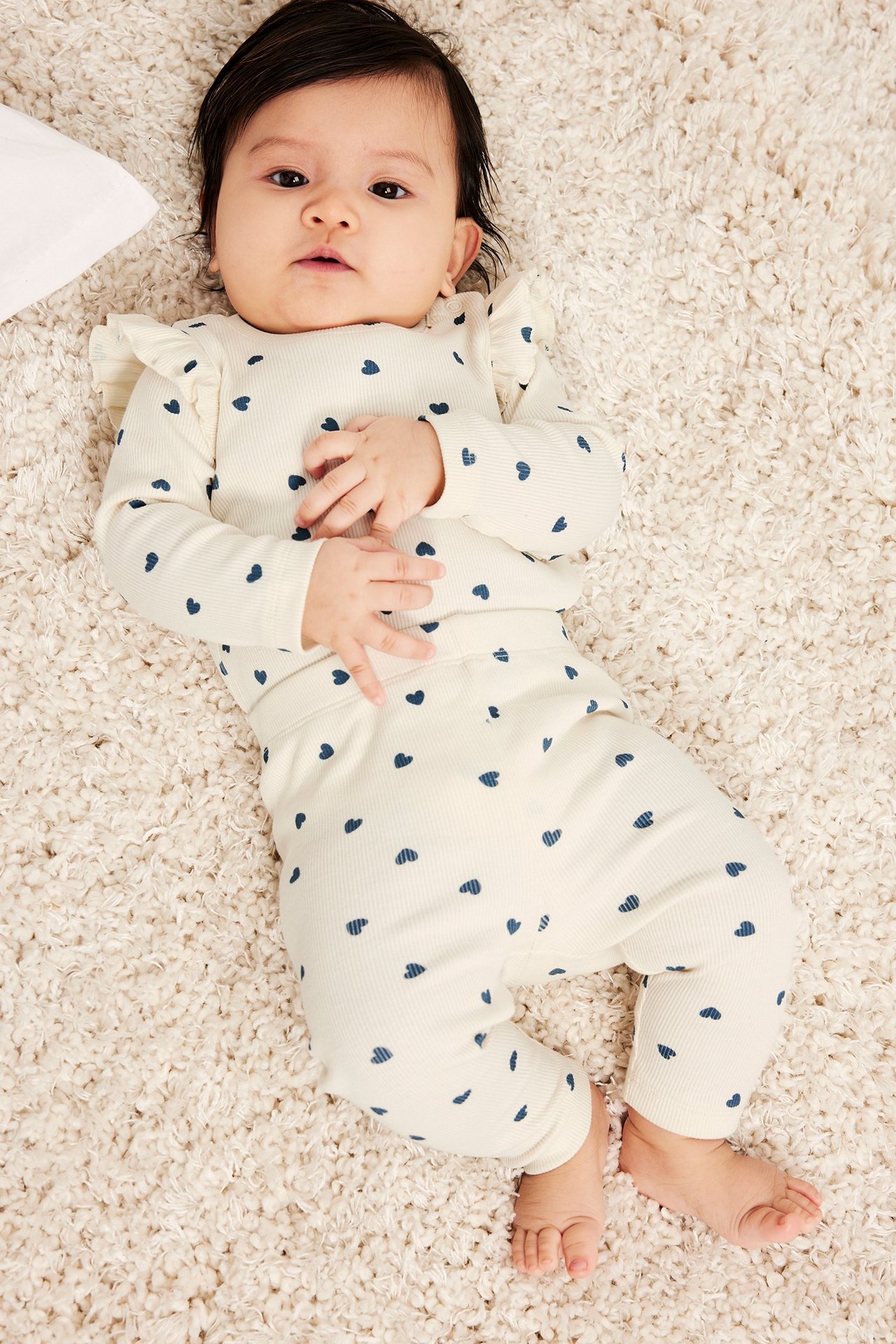 Widok z przodu: dziecko w białych prążkowanych legginsach i bluzce w niebieskie serca.
