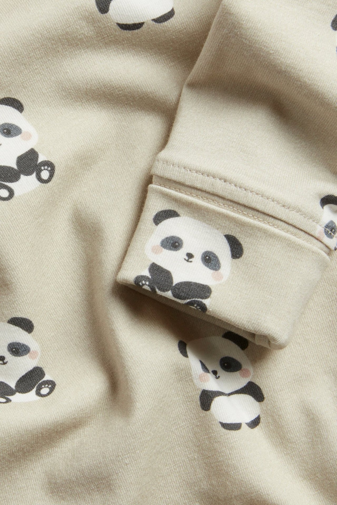 Lähikuva beigestä puuvillaisesta pitkähihaisesta vauvanbodysta, jossa on mustavalkoinen pandaprintti hihassa.