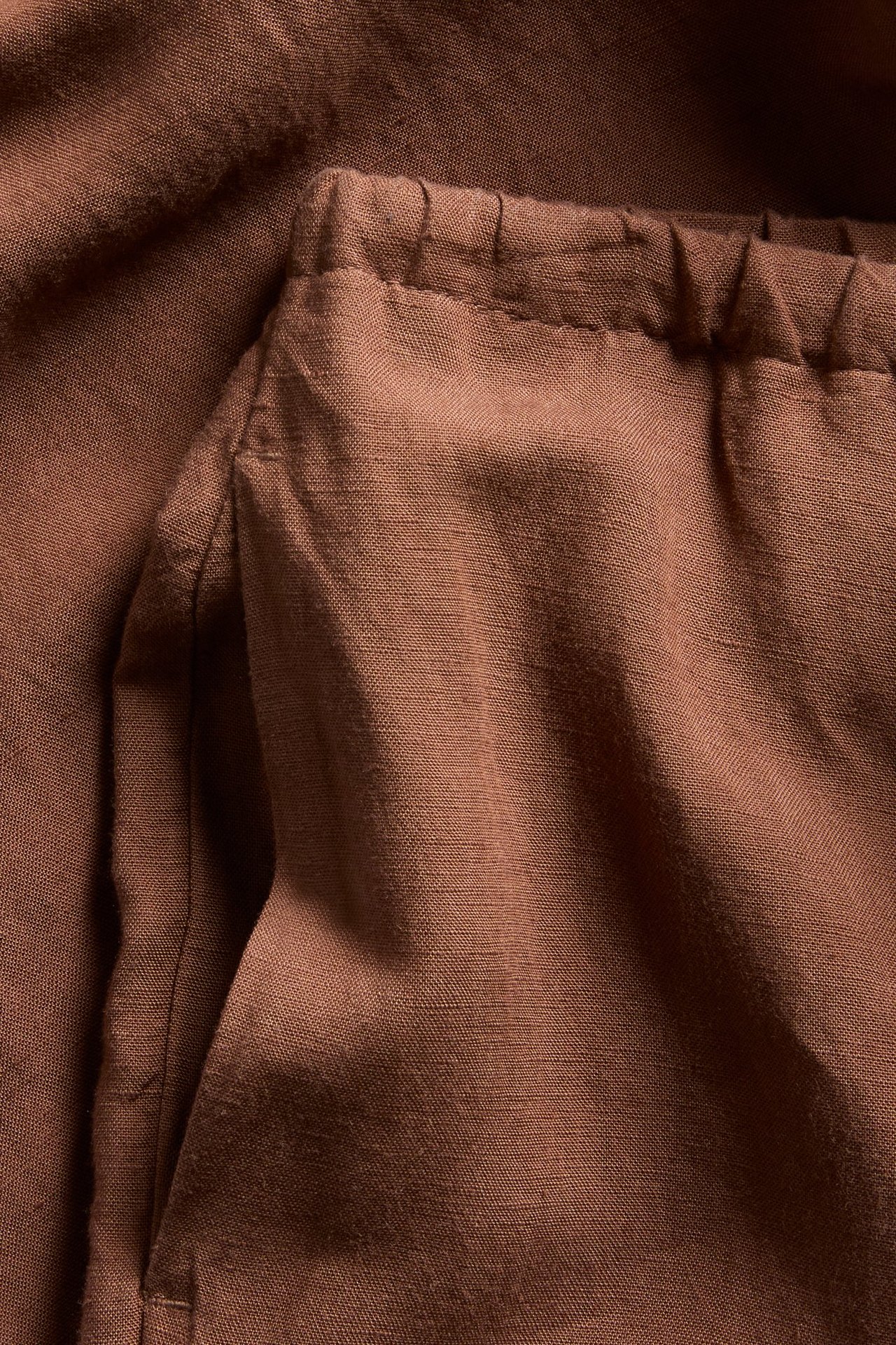 Närbild av bruna linnebyxor med resår i midjan och sidoficka.