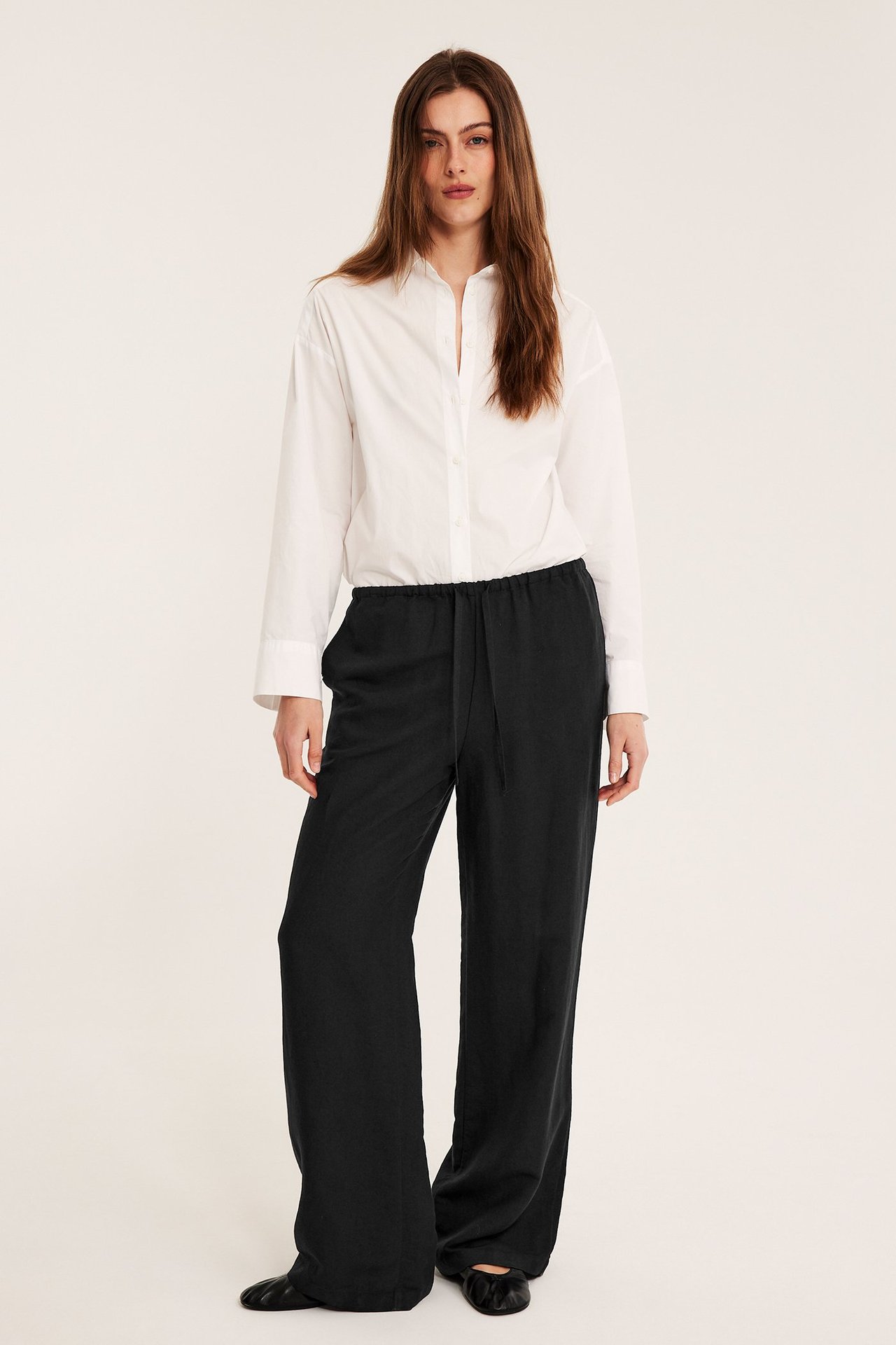 Edestä kuvattu nainen yllään mustat pellavasekoitehousut nyörillä ja valkoinen kauluspaita.