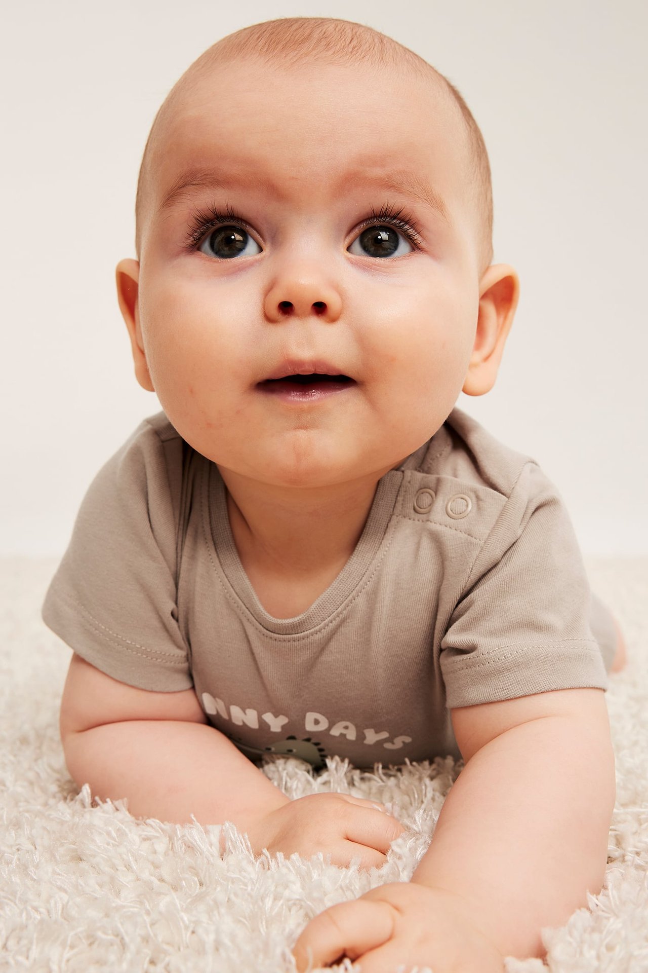 Widok z przodu: Niemowlę w beżowym body z krótkim rękawem, z napami na ramieniu i nadrukiem.