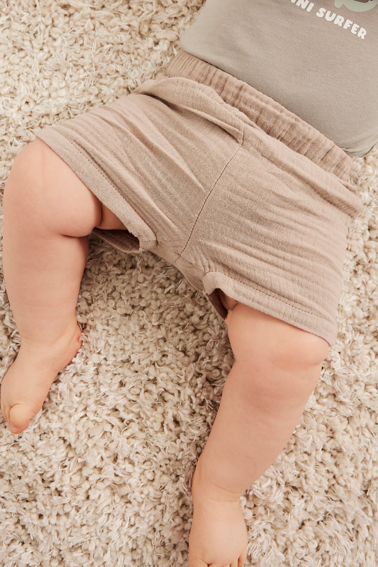 Widok z góry na dziecko w jasnobeżowych prążkowanych szortach i szarym topie na dywanie.