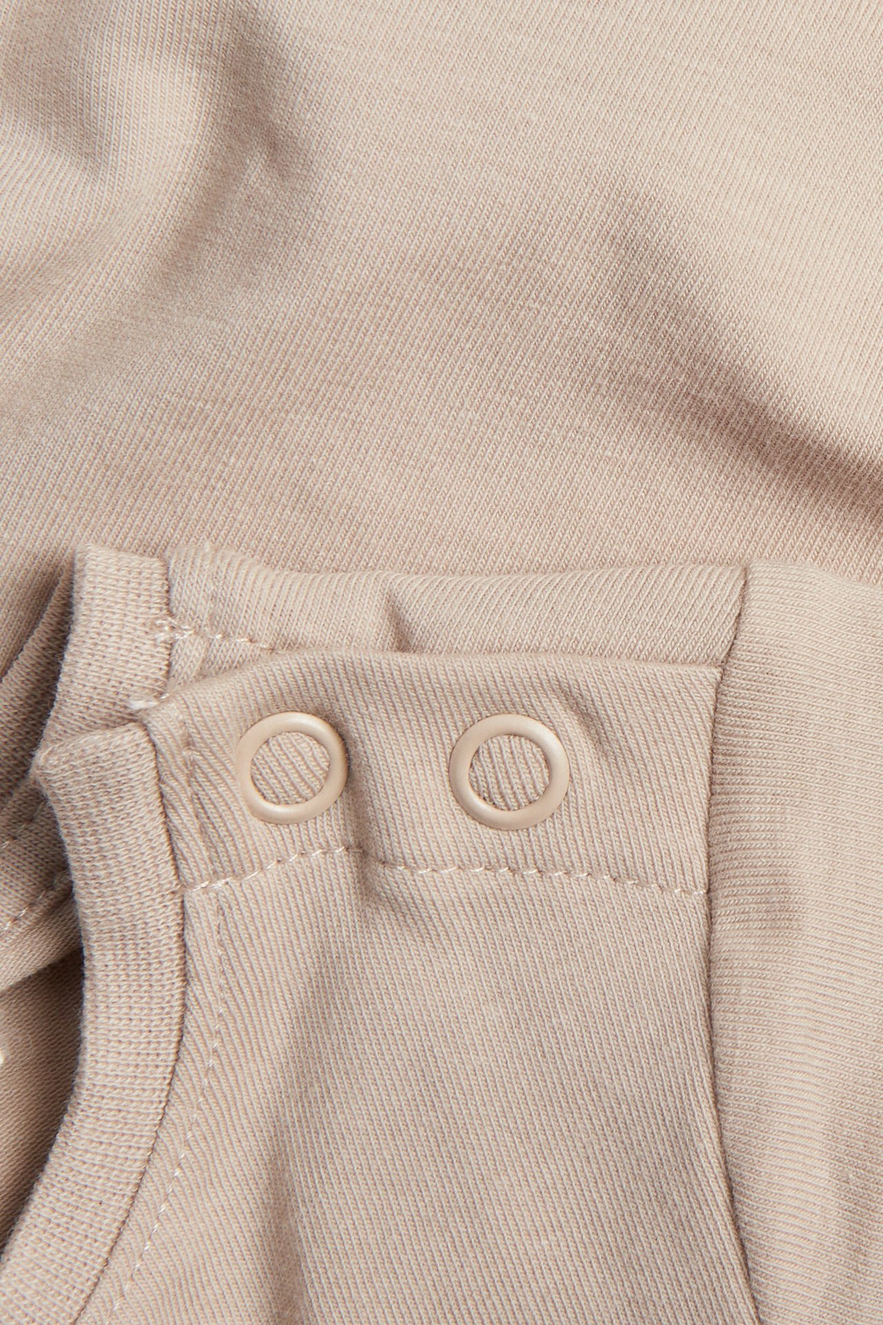 Lähikuva beigestä single jersey -vauvanbodytistä, jossa kaksi vaaleanbeigettä painonappia olalla.