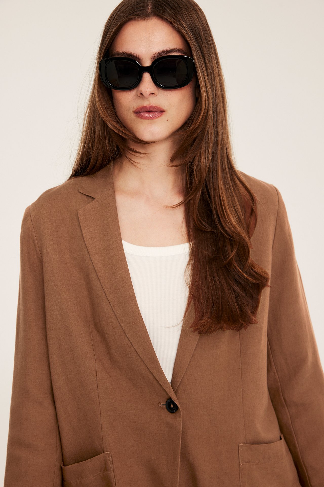 Edestä: nainen ruskeassa pellavasekoitebleiserissä napilla, valkoisessa topissa ja mustissa aurinkolaseissa.