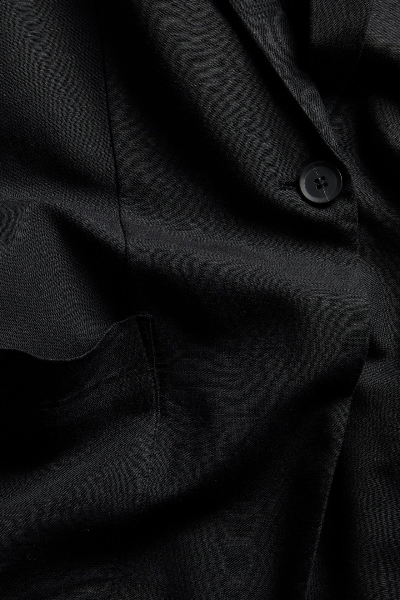 Zbliżenie czarnej marynarki z mieszanki lnu, z jednym guzikiem i widoczną naszytą kieszenią.