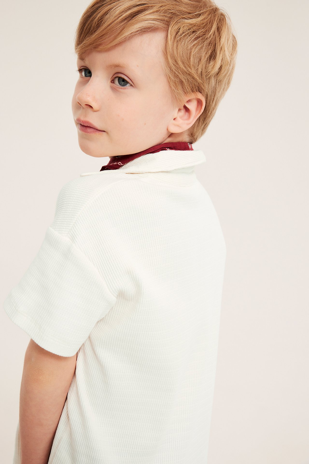 Nærbilde av et barn i en offwhite strukturert bomullspiké og en rød mønstret bandana.