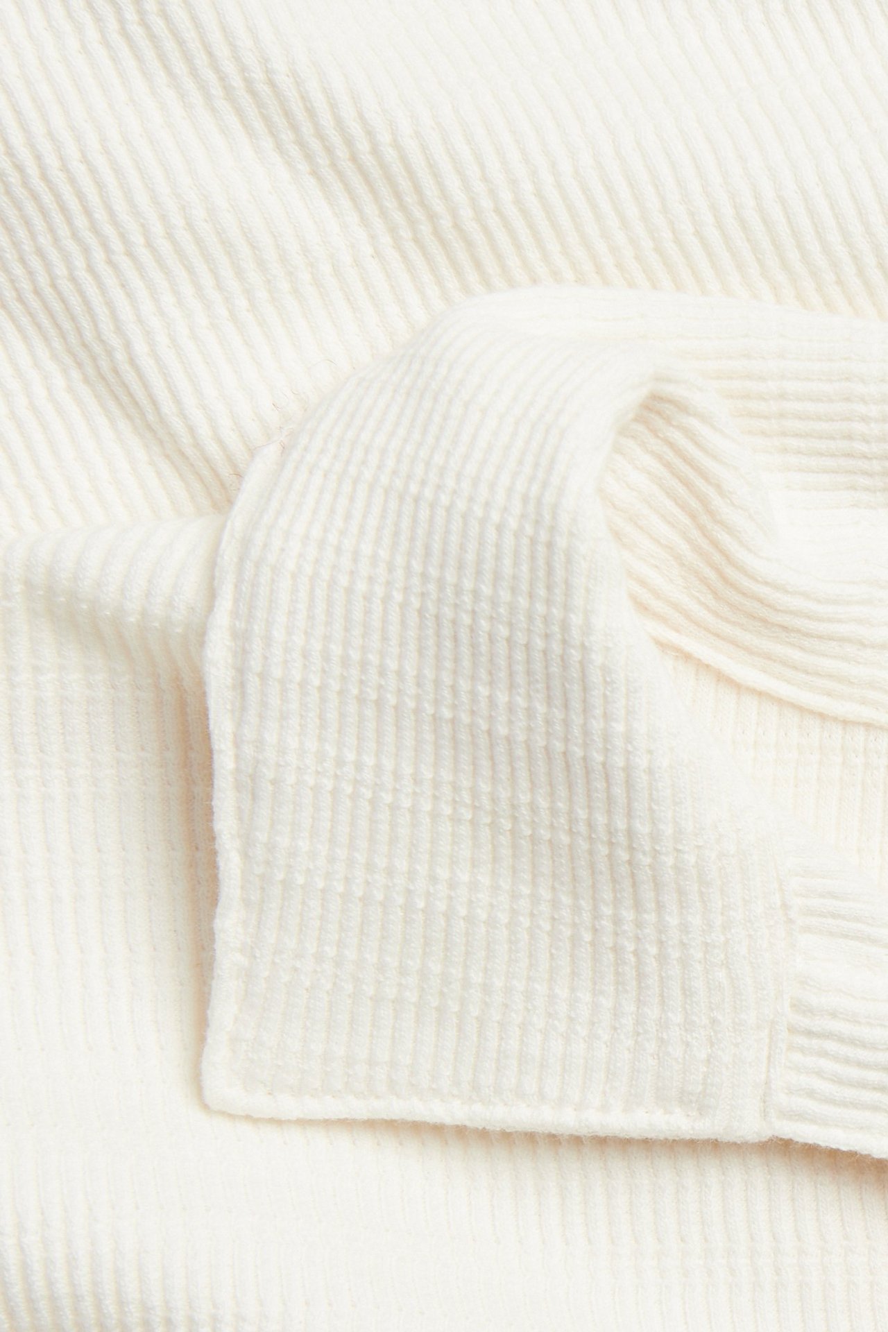 Zbliżenie na off-white fakturowaną dzianinę bawełnianej koszulki polo.