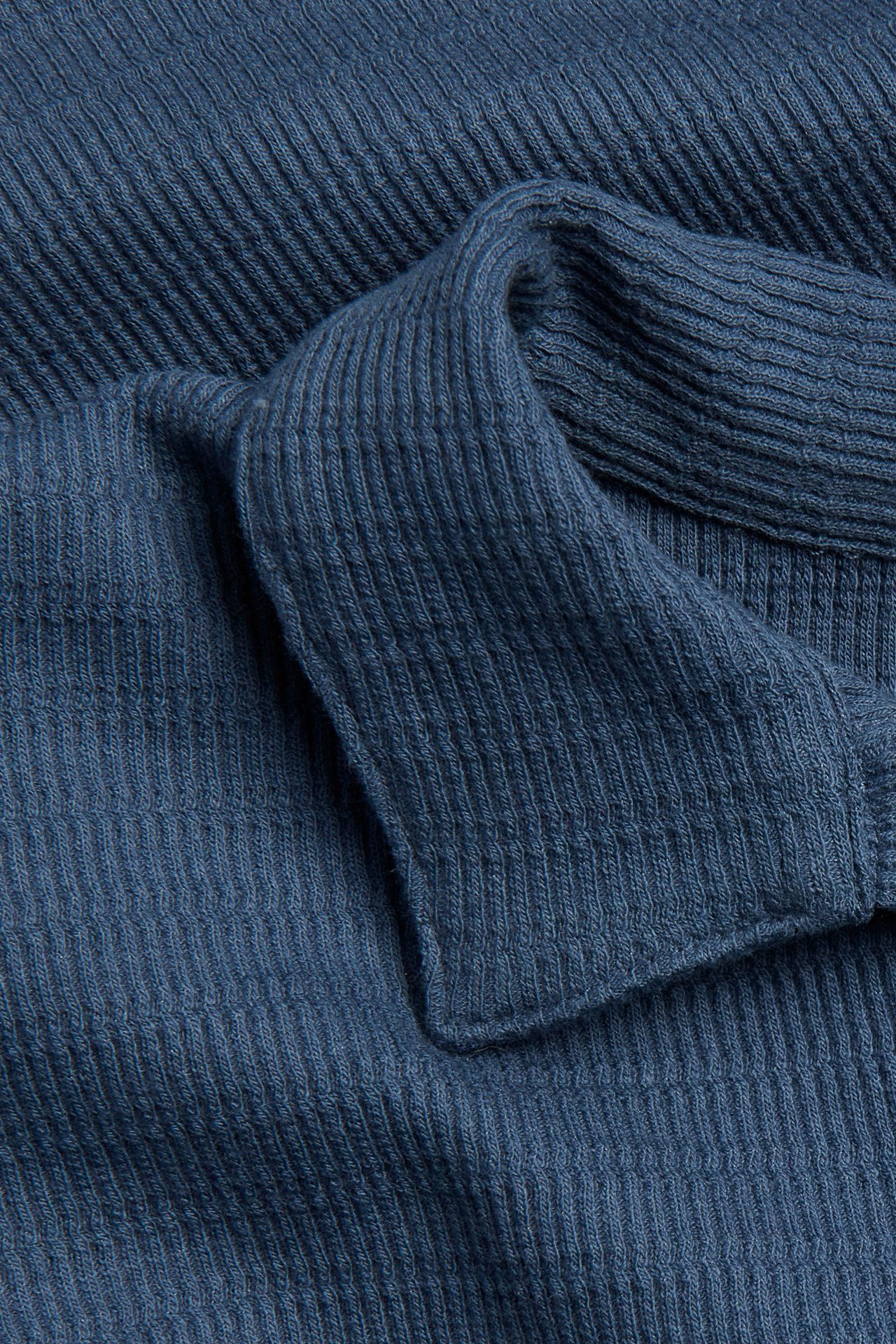 Zbliżenie niebieskiej, strukturalnej koszulki polo z bawełnianego dżerseju, ukazujące kołnierz.