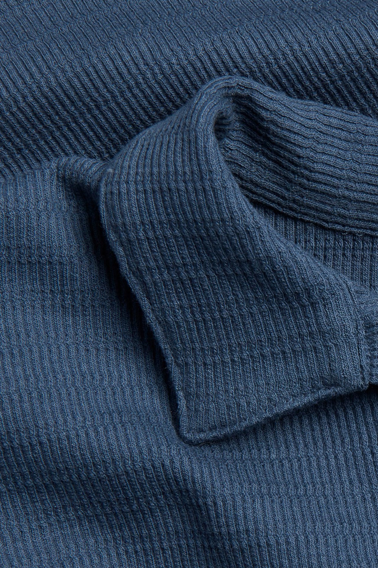 Zbliżenie niebieskiej, strukturalnej koszulki polo z bawełnianego dżerseju, ukazujące kołnierz.