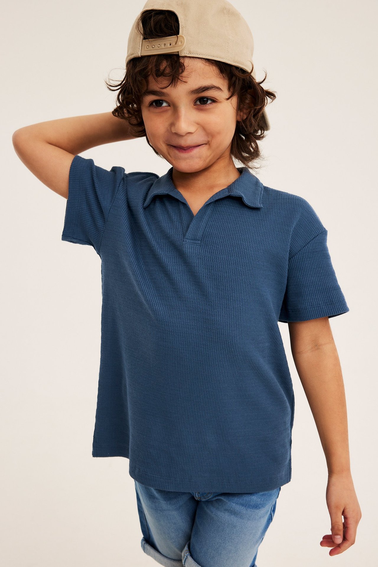 Z przodu: dziecko w niebieskiej prążkowanej koszulce polo, jasnoniebieskich szortach i beżowej czapce.